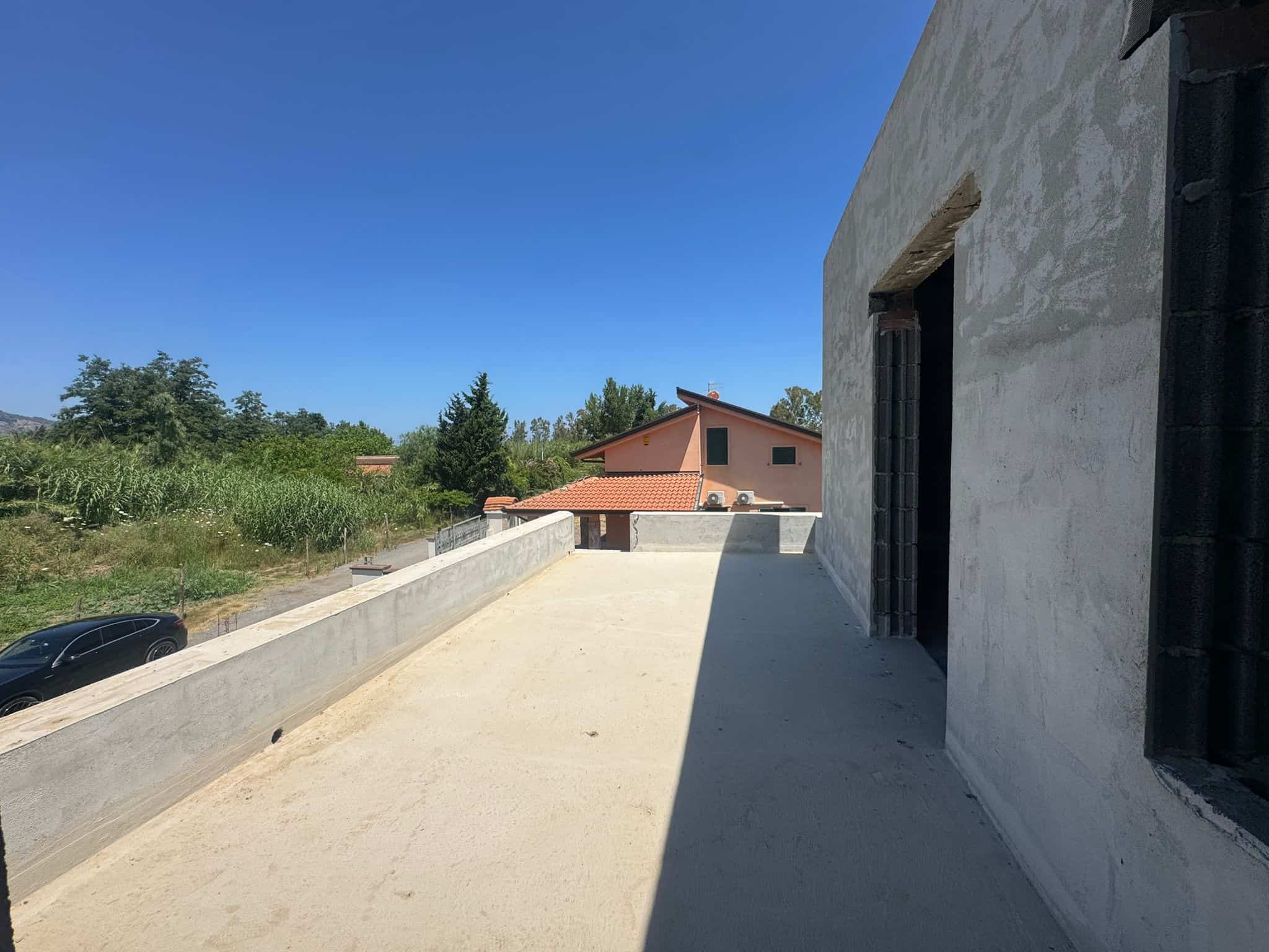 Balcone di una casa in costruzione con vista su un paesaggio verde e cielo azzurro.
