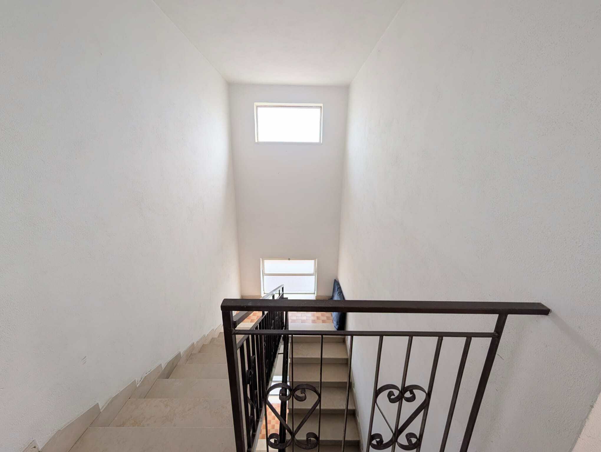 Scalinata interna con ringhiera in ferro battuto e finestra luminosa in alto, ambiente luminoso e minimalista.