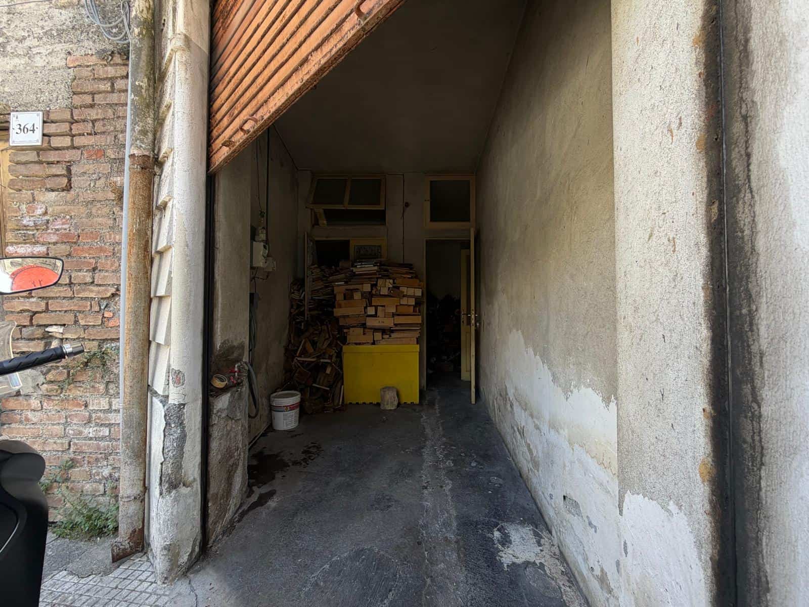 Ingresso di un garage o deposito con pareti in cemento e legno, spazio interno con materiali di costruzione e attrezzi.