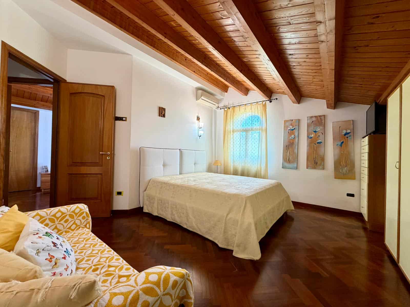 Camera da letto spaziosa con soffitto in legno, pareti bianche e arredi moderni, ideale per una villa in vendita a Terme Vigliatore.