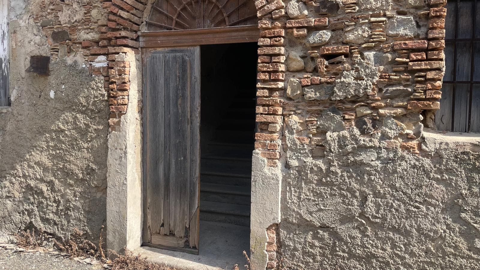 Porta in legno rustica inserita in un muro di pietra antica, con arcata in mattoni sopra l'ingresso, che evidenzia un'architettura storica e tradizionale.