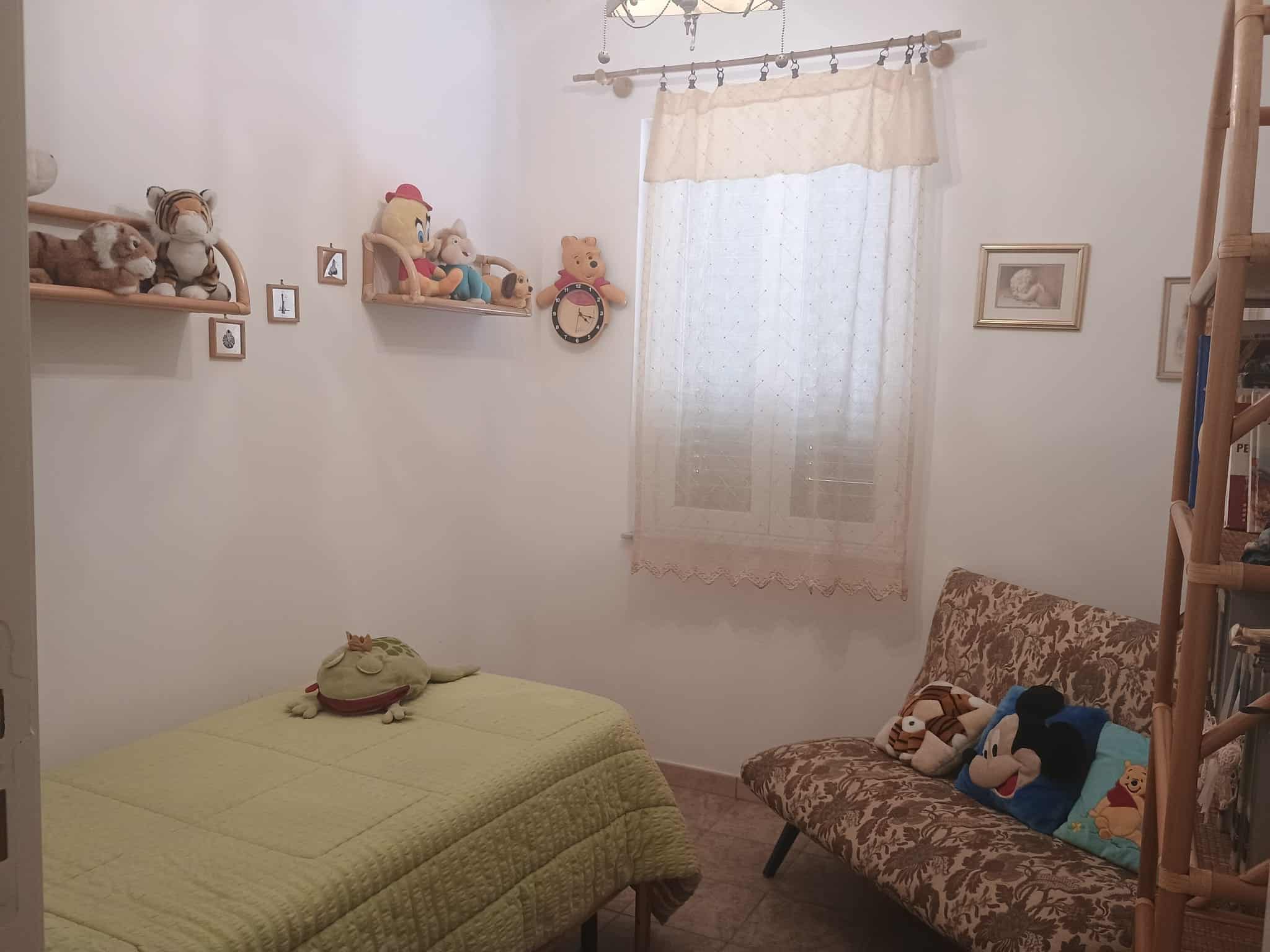 Letto per bambini con decorazioni giocattolo e tende leggere, in una stanza accogliente e luminosa, decorata con peluche e quadri alle pareti, ideale per un ambiente di riposo e gioco.