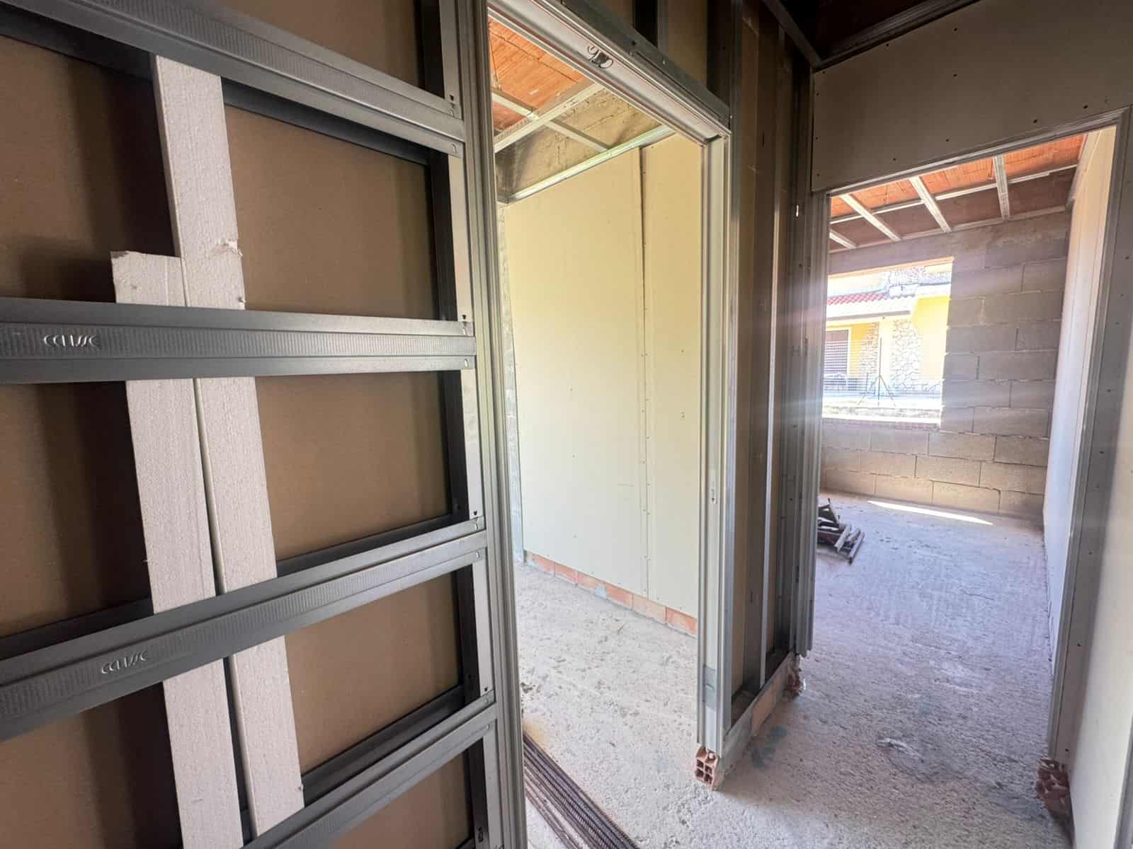 Vista di un ingresso di un edificio in costruzione con struttura in acciaio e pareti in fase di finitura, luce naturale che entra dall'esterno.