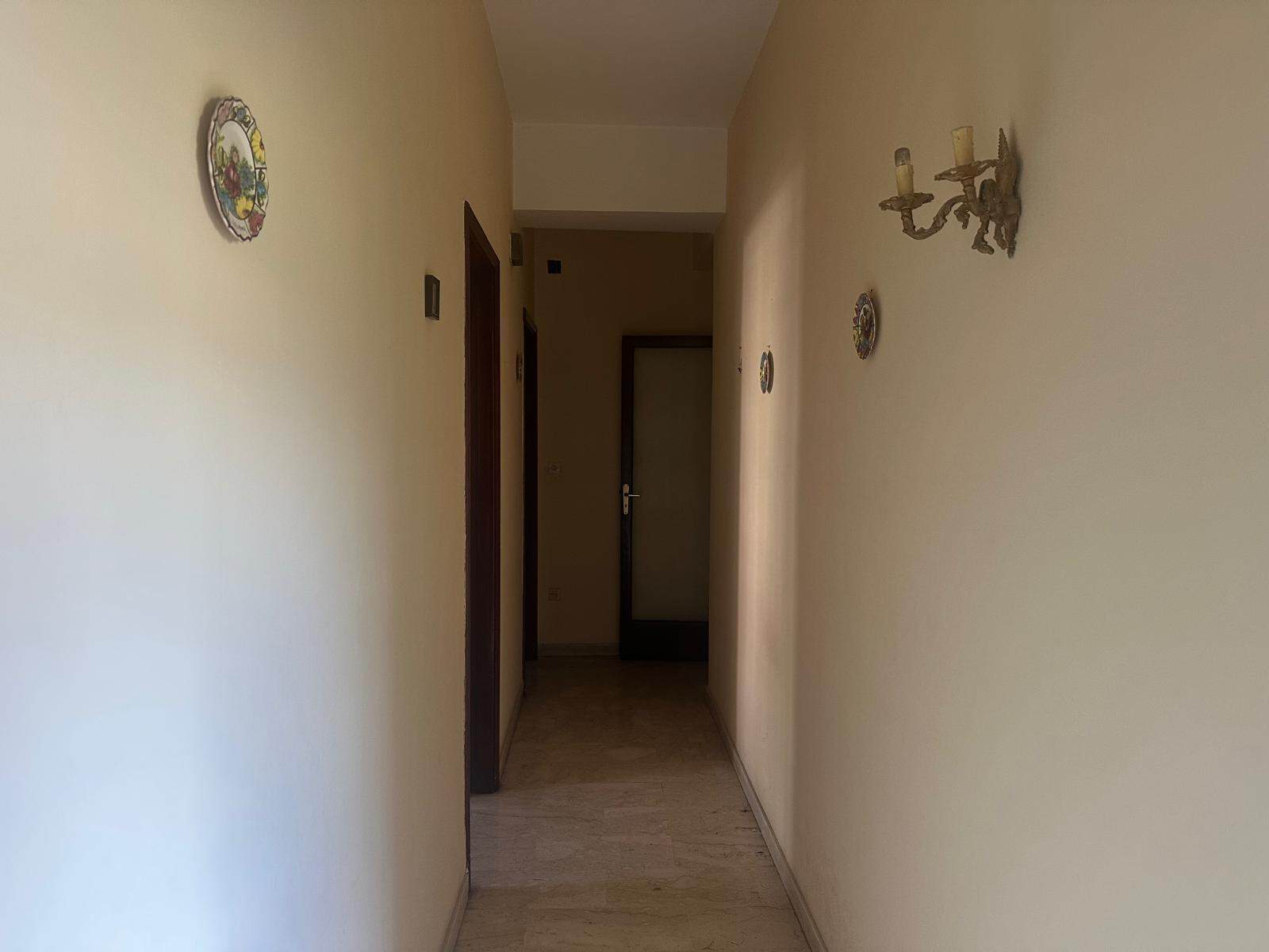 Corridoio interno di un appartamento con pareti beige, decorazioni floreali e applique luminose, ambiente luminoso e accogliente.