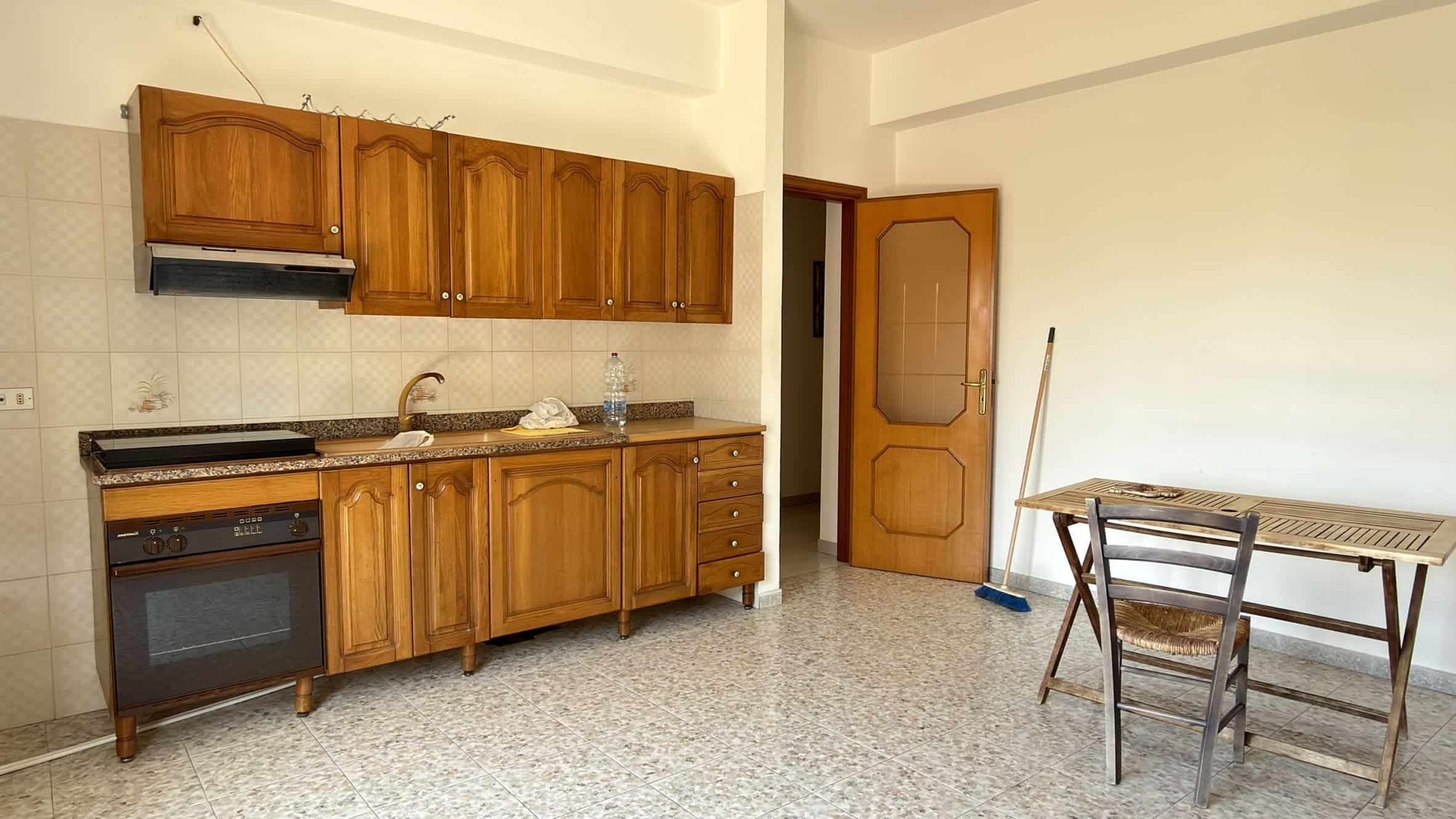 Cucina semplice con mobili in legno, piano di lavoro in granito e elettrodomestici di base in un appartamento a NextCasa.