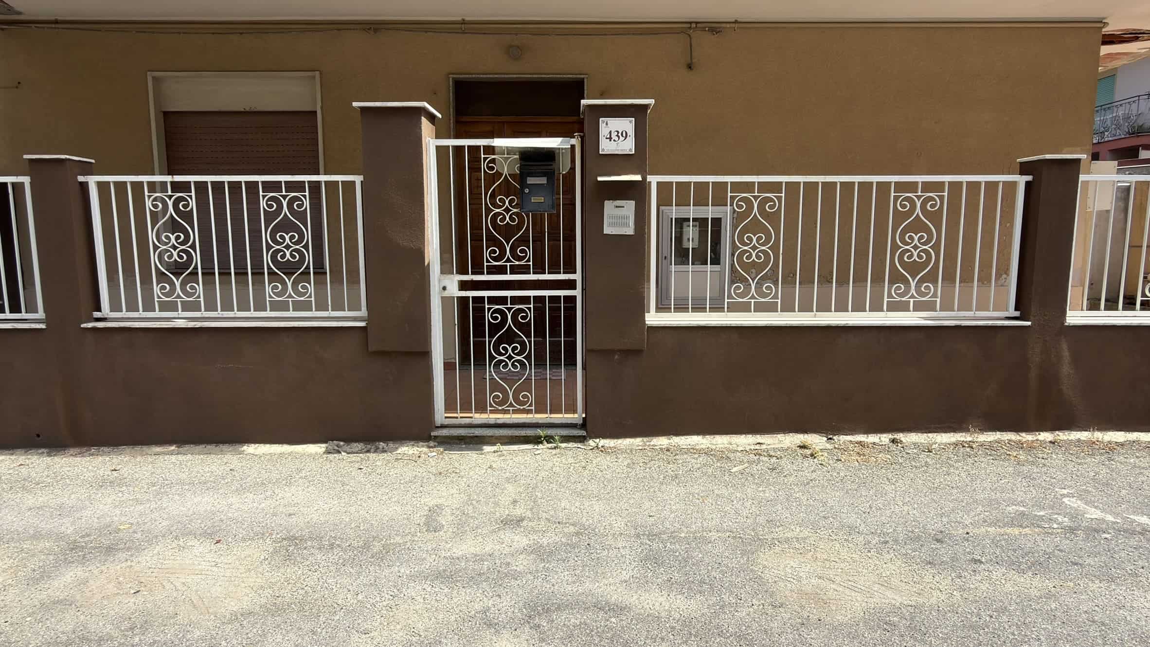 Cancello e recinzione in ferro battuto bianco davanti a una casa moderna con pareti beige.