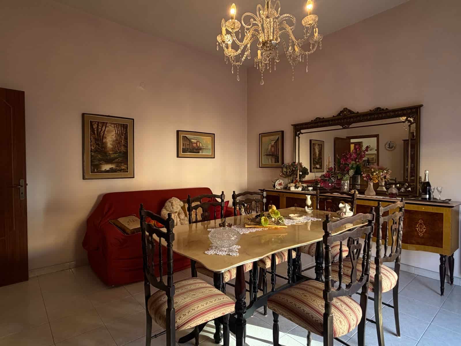 Elegante sala da pranzo con tavolo in legno, sedie imbottite, grande specchio e lampadario in cristallo in un appartamento a Barcellona P.G.