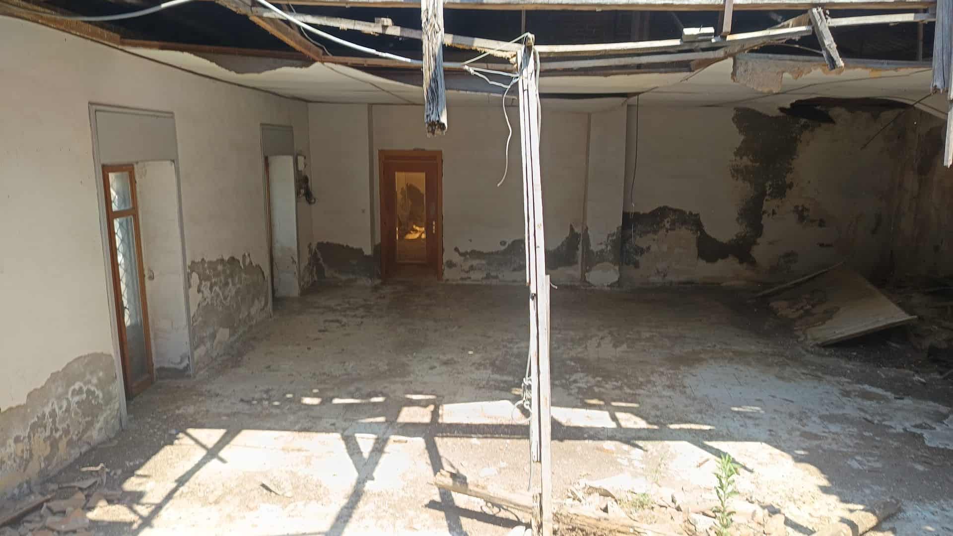 Interno di un locale commerciale in ristrutturazione con pareti danneggiate e pavimento in cemento.