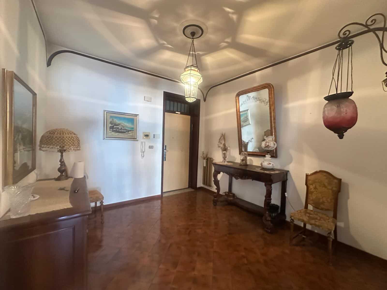 Interno di un soggiorno elegante con mobili d'epoca, specchio grande e lampada sospesa, atmosfera calda e accogliente.