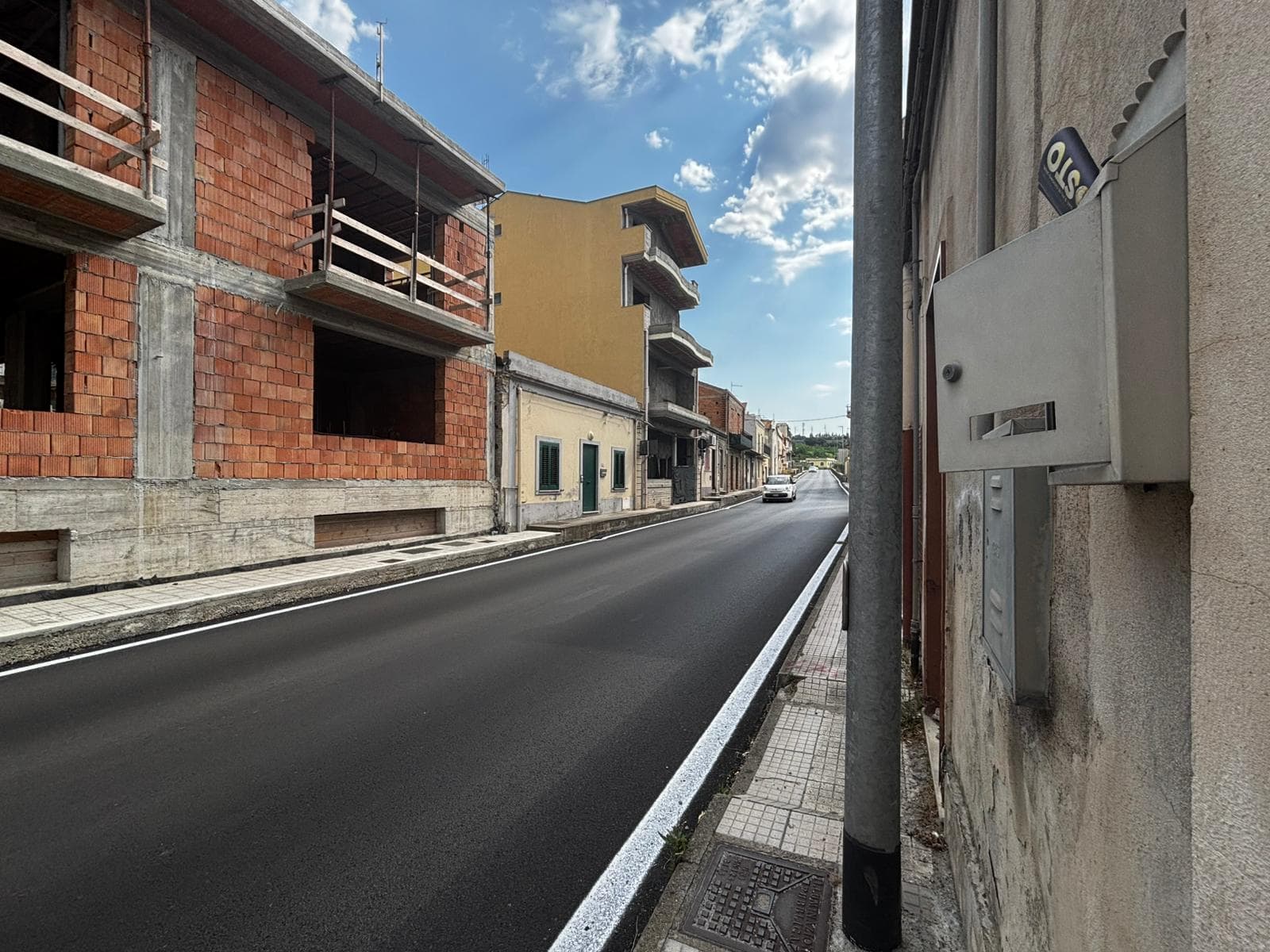 Strada urbana con edifici in costruzione e cielo sereno, vista laterale, in un quartiere residenziale.
