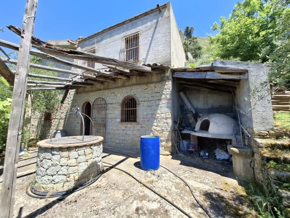 Pannello solare e forno a legna in cortile esterno di una casa rurale in pietra, con ambiente naturale e vegetazione circostante, in Italia.