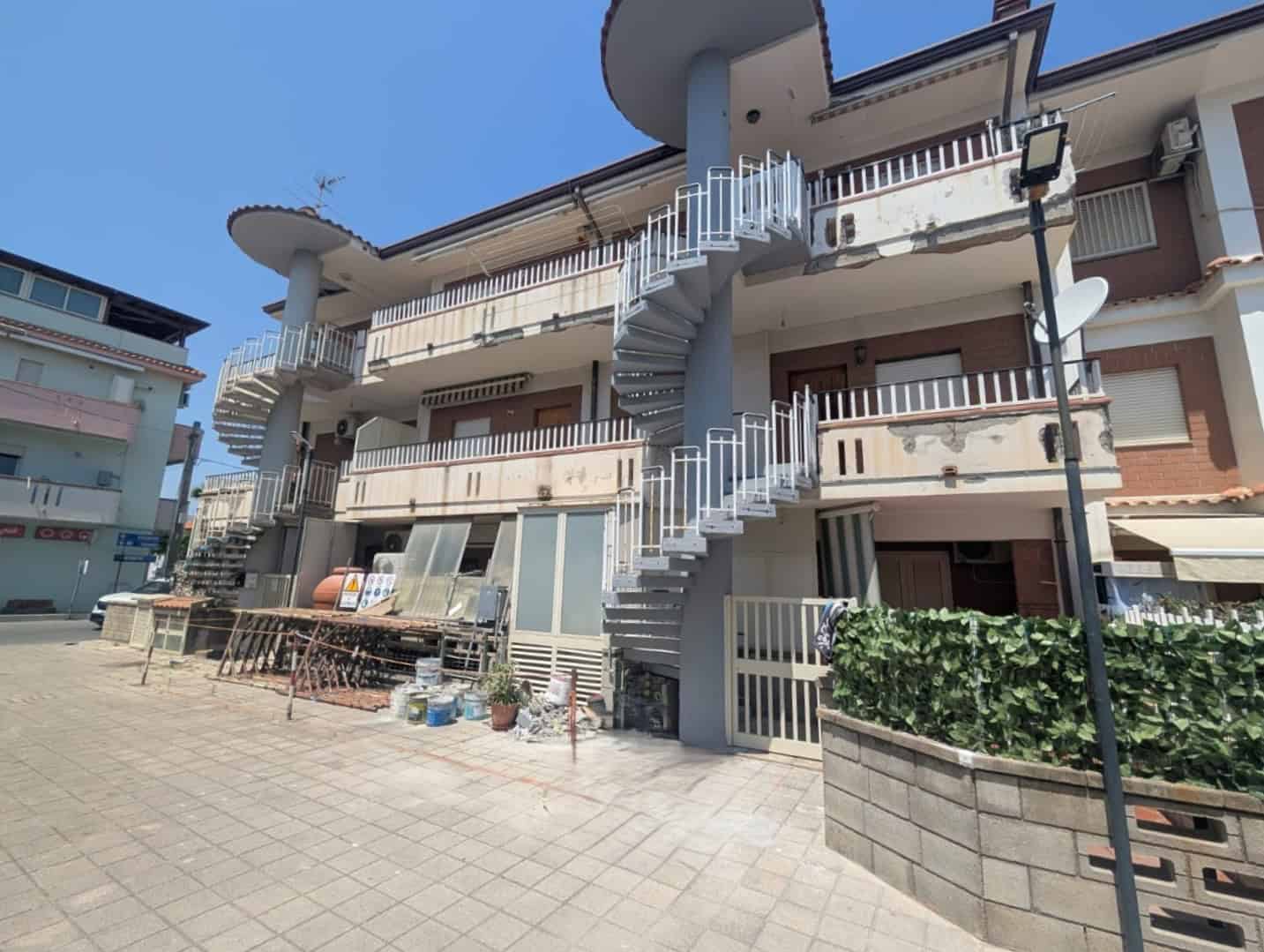 Ponteggio e lavori di ristrutturazione su edificio residenziale con scale a chiocciola esterne, in fase di manutenzione e restauro, in un'area urbana.