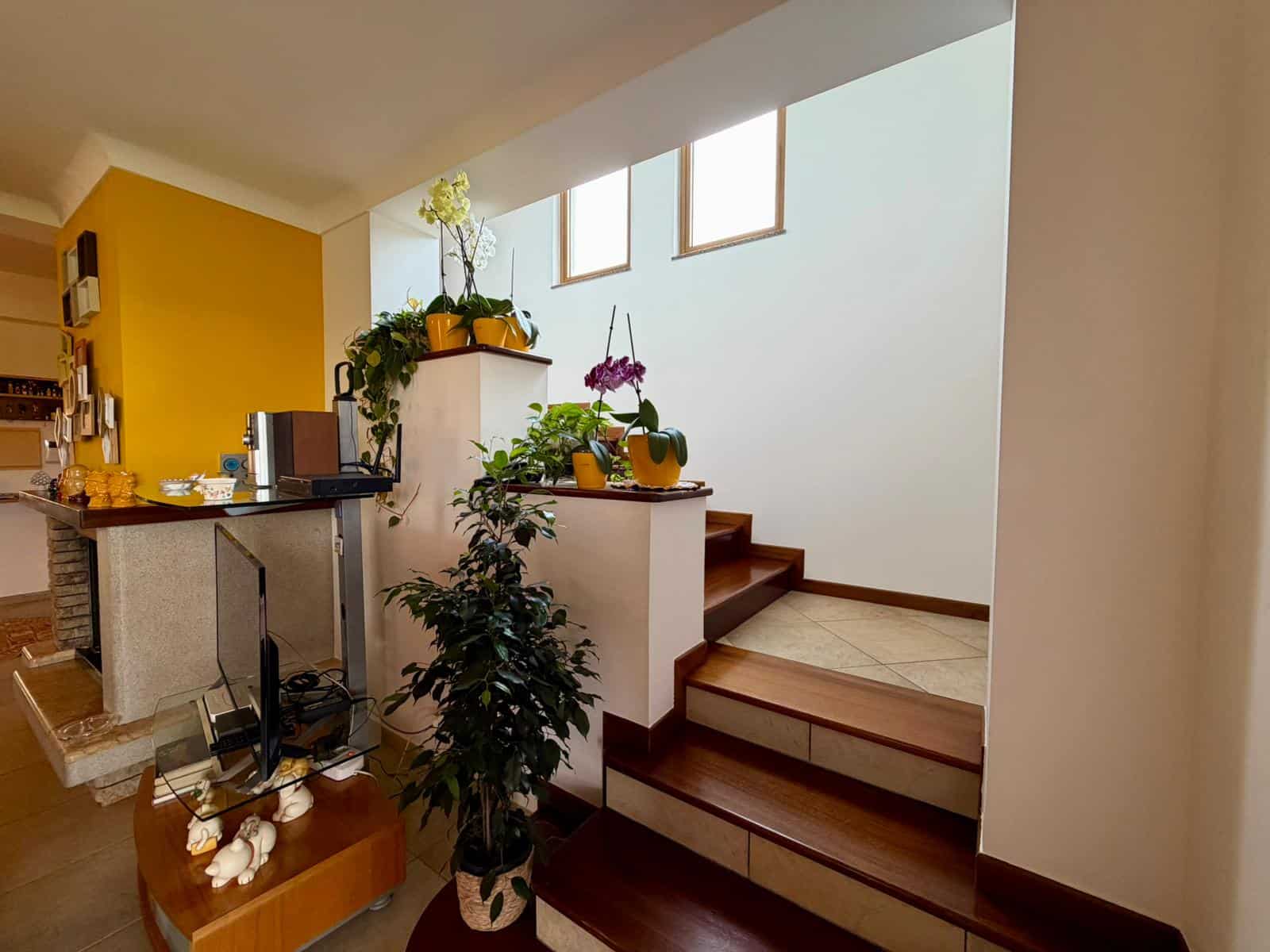 Interno di una villa con scale in legno e decorazioni floreali, ambiente luminoso e accogliente.
