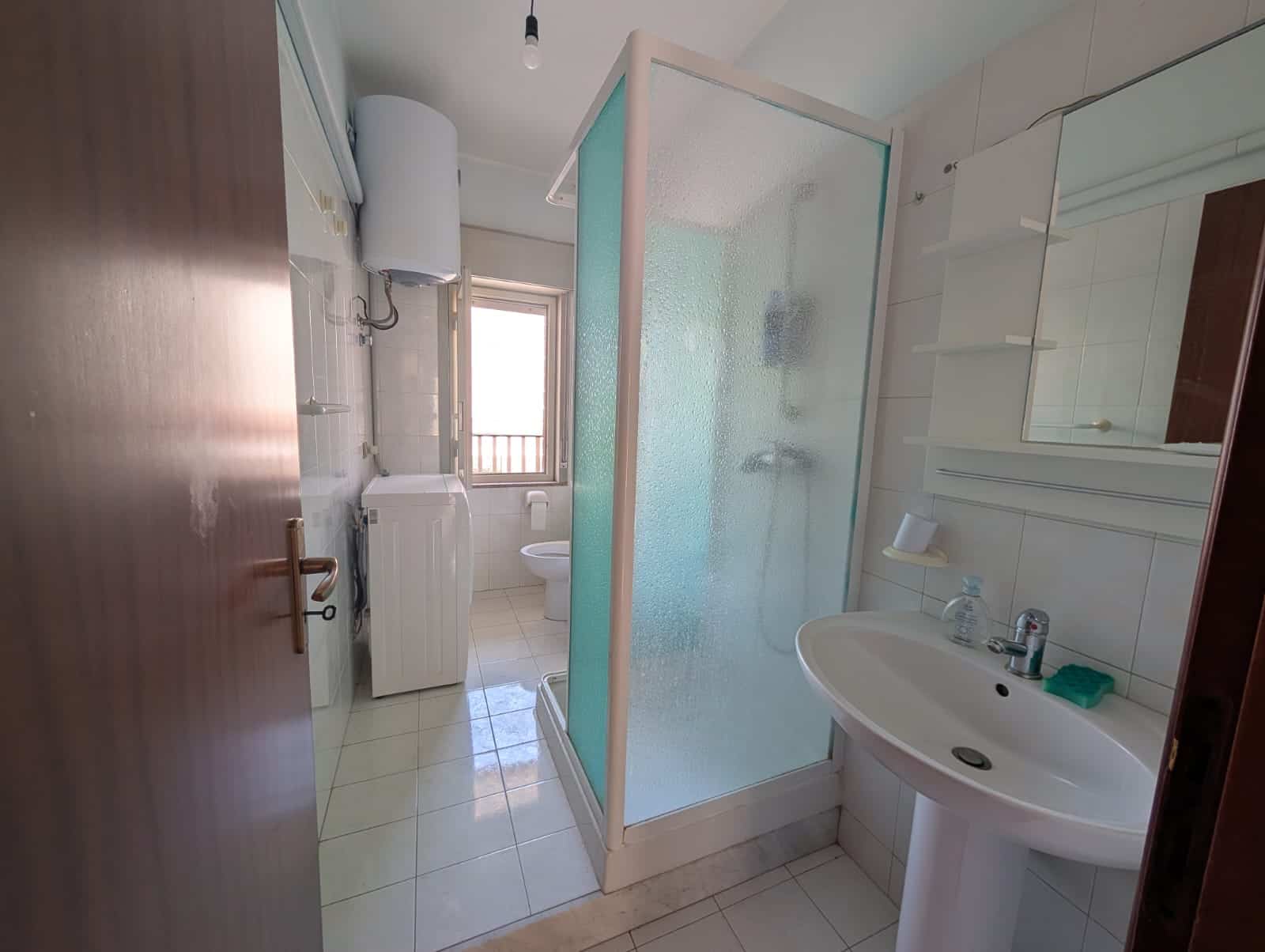 Bagno con doccia, lavabo e lavatrice in un ambiente compatto.
