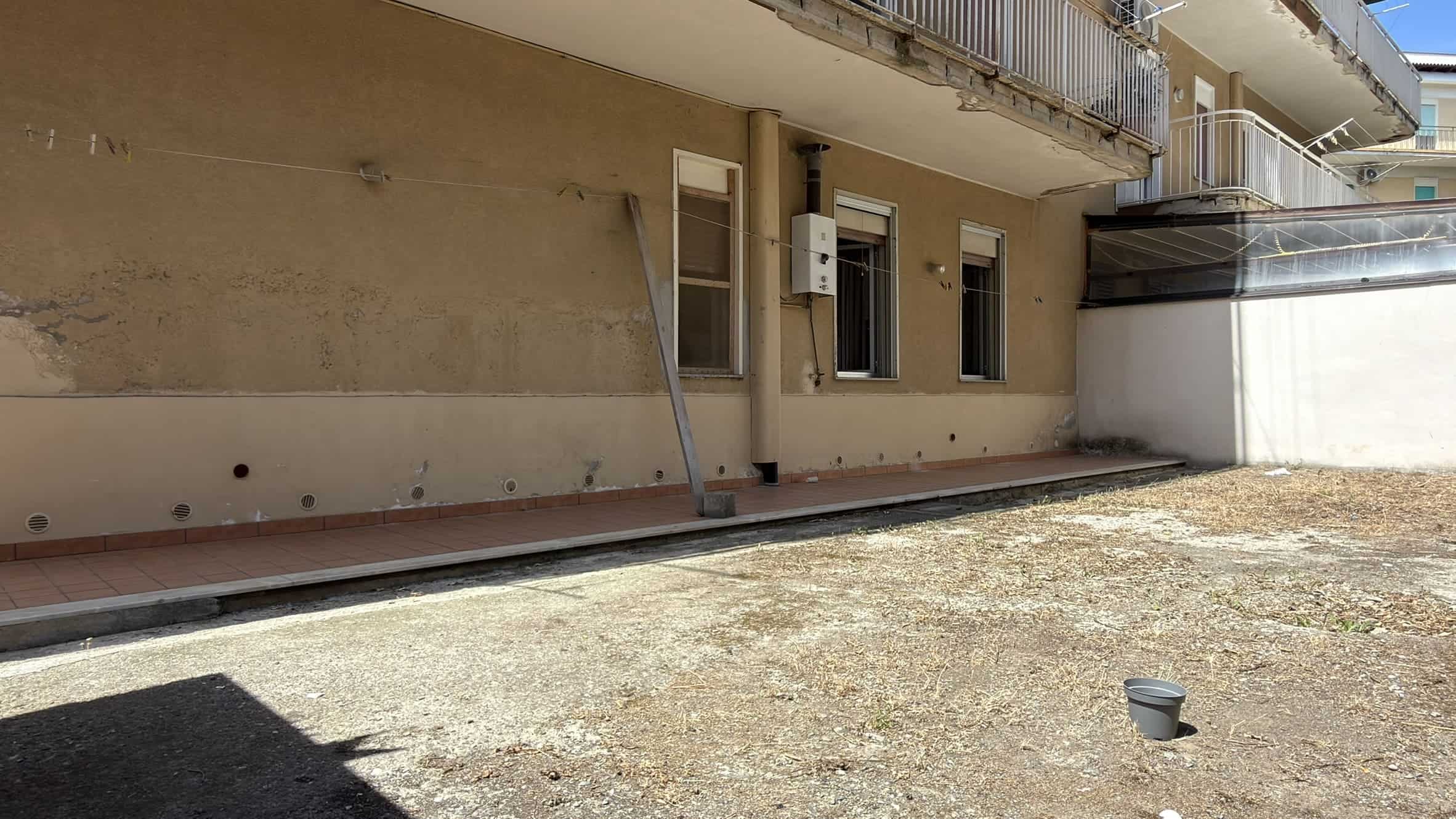 Facciata di un edificio residenziale con balconi e finestre, vista da strada con area esterna non pavimentata.