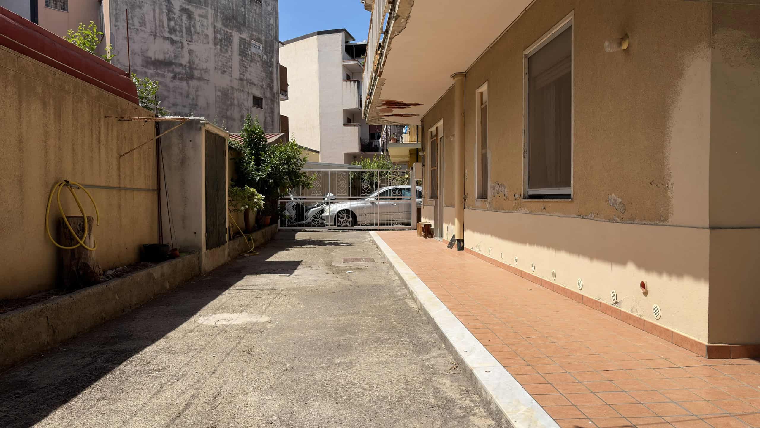 Vicolo residenziale con parcheggio e edificio in stile semplice, illuminato dal sole, in zona urbana.