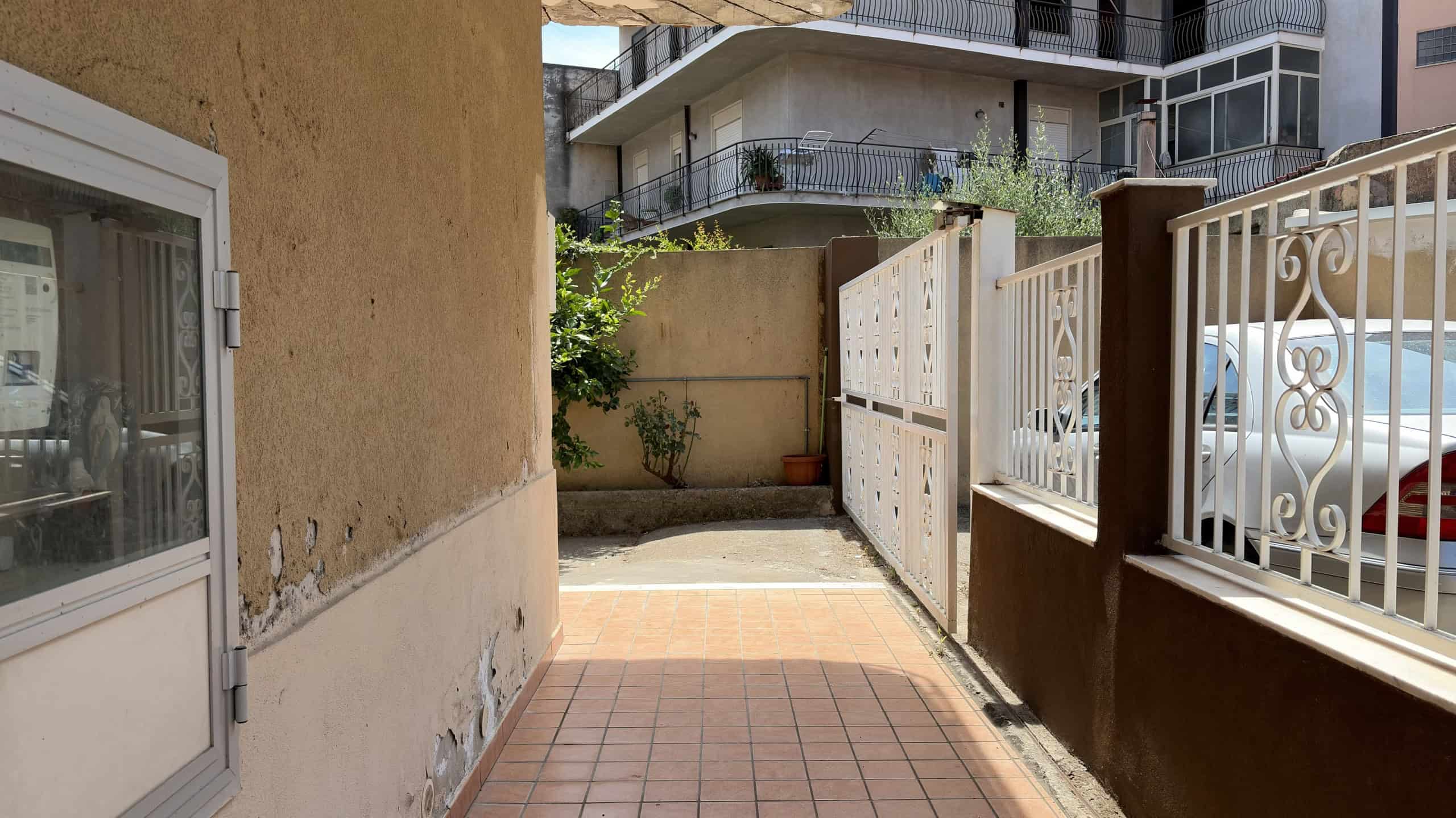 Ingresso di un cortile condominiale con cancello e pavimentazione in piastrelle, vista di un'area esterna privata.