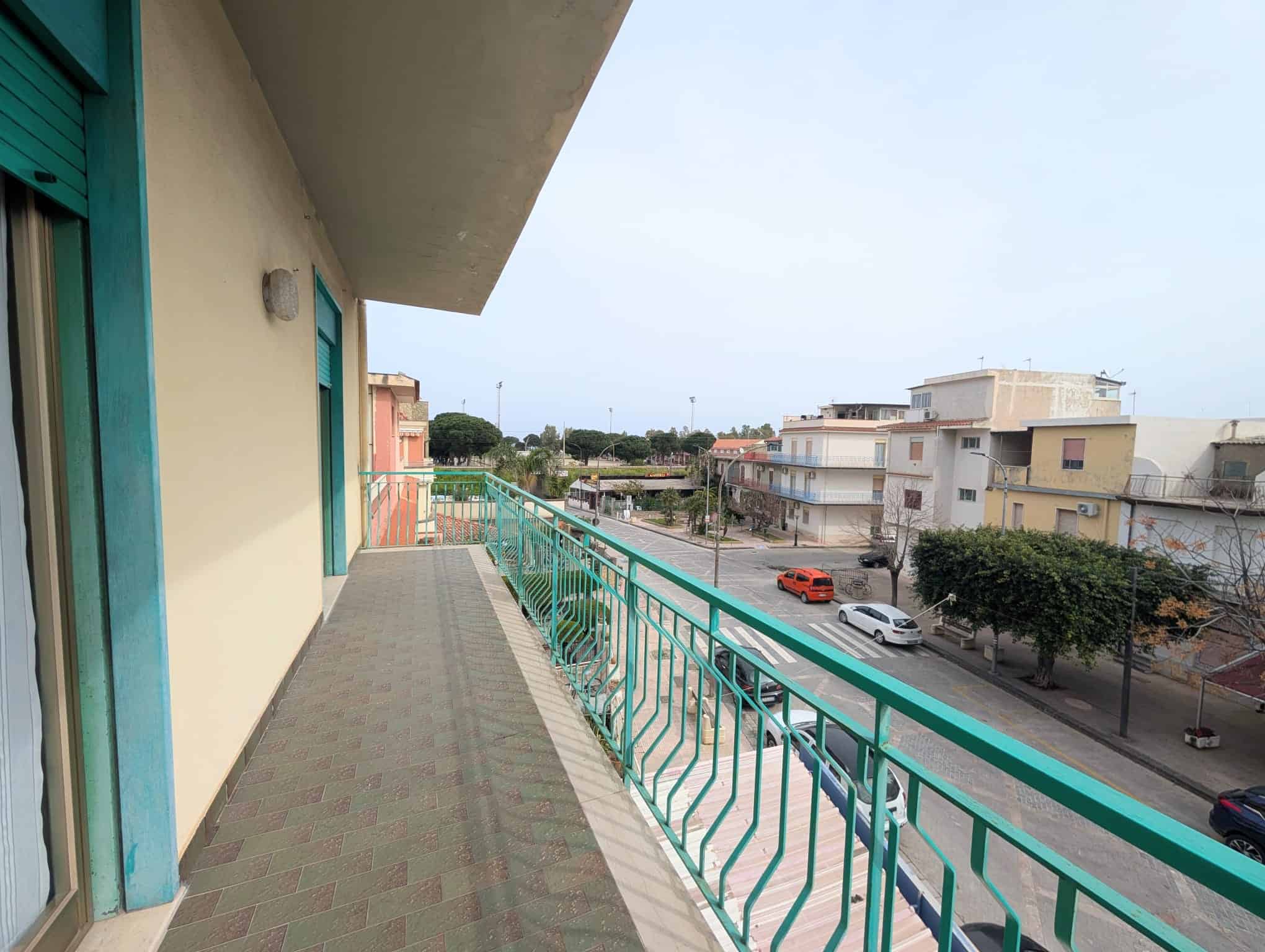 Balcone di un appartamento con vista sulla strada e edifici circostanti, in zona urbana.
