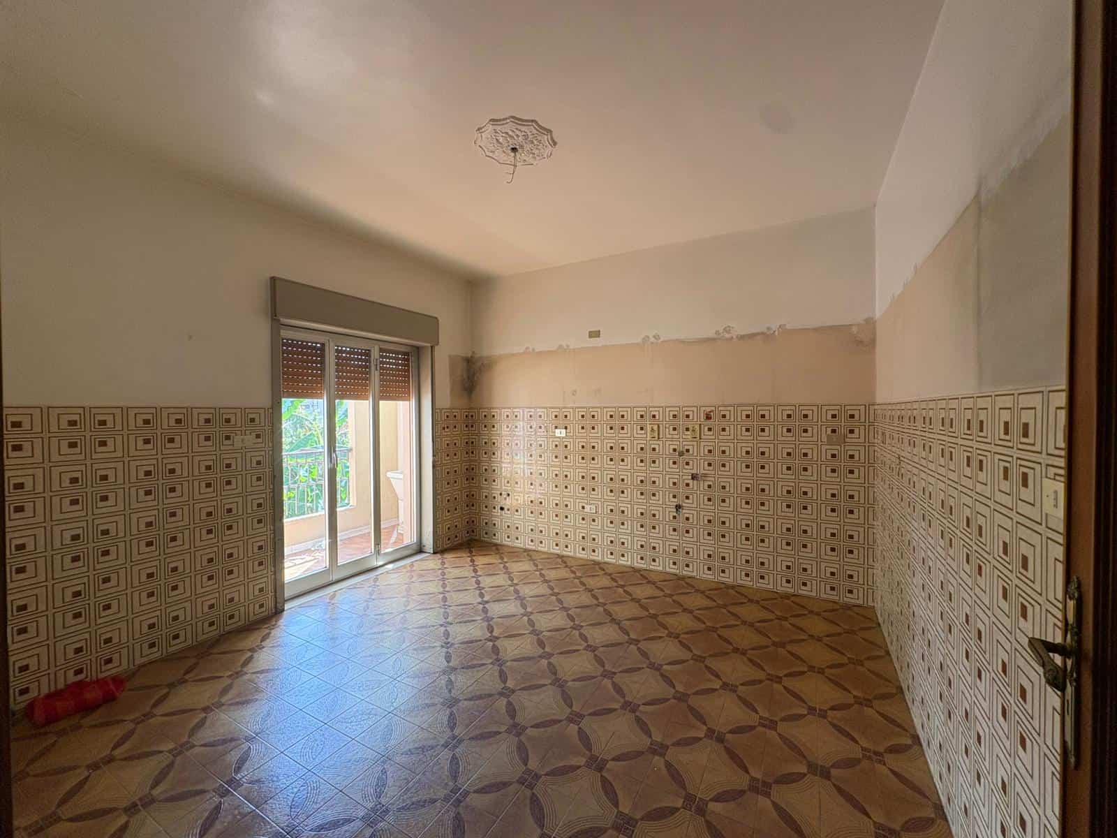 Stanza vuota in vendita in Via Nino Bixio 2, Merì, con pareti parzialmente ristrutturate e accesso a balcone.