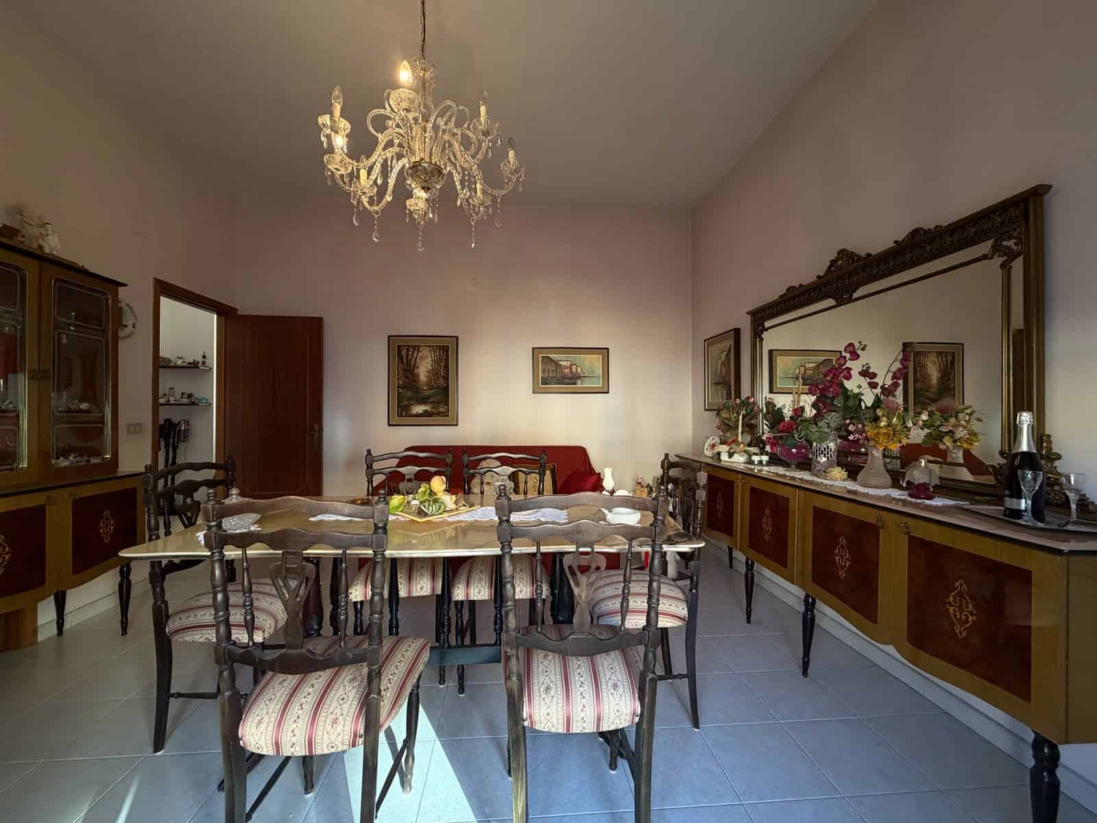 Interno di un soggiorno elegante con tavolo da pranzo, sedie, grande specchio e lampadario in cristallo.