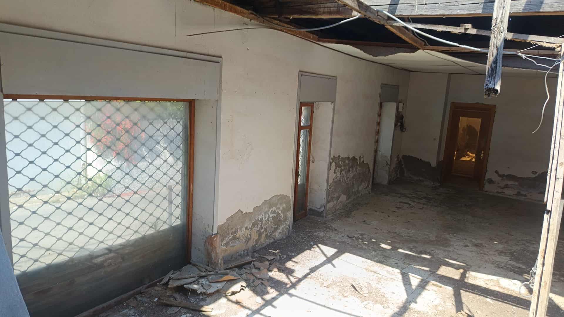 Interno di un locale commerciale in ristrutturazione con pareti danneggiate e pavimento sporco.
