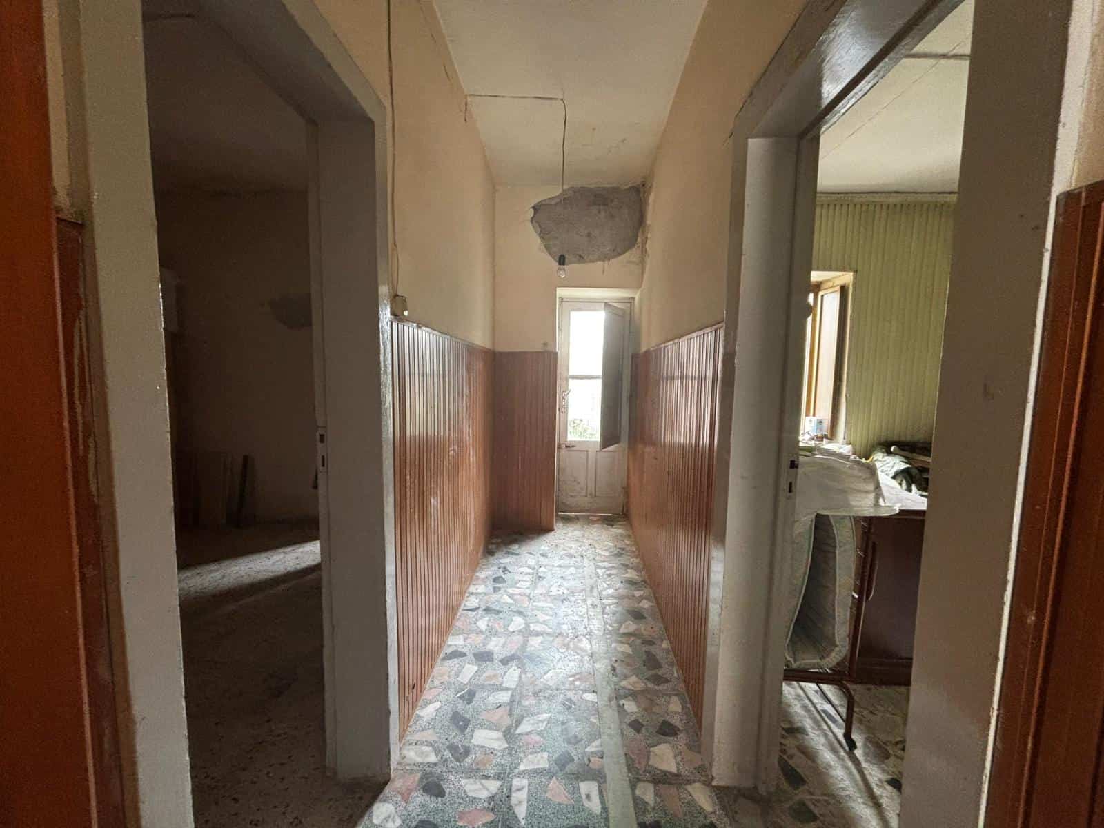 Corridoio in un appartamento in stile vintage con pareti in legno e soffitto danneggiato, luce naturale proveniente dalla finestra.