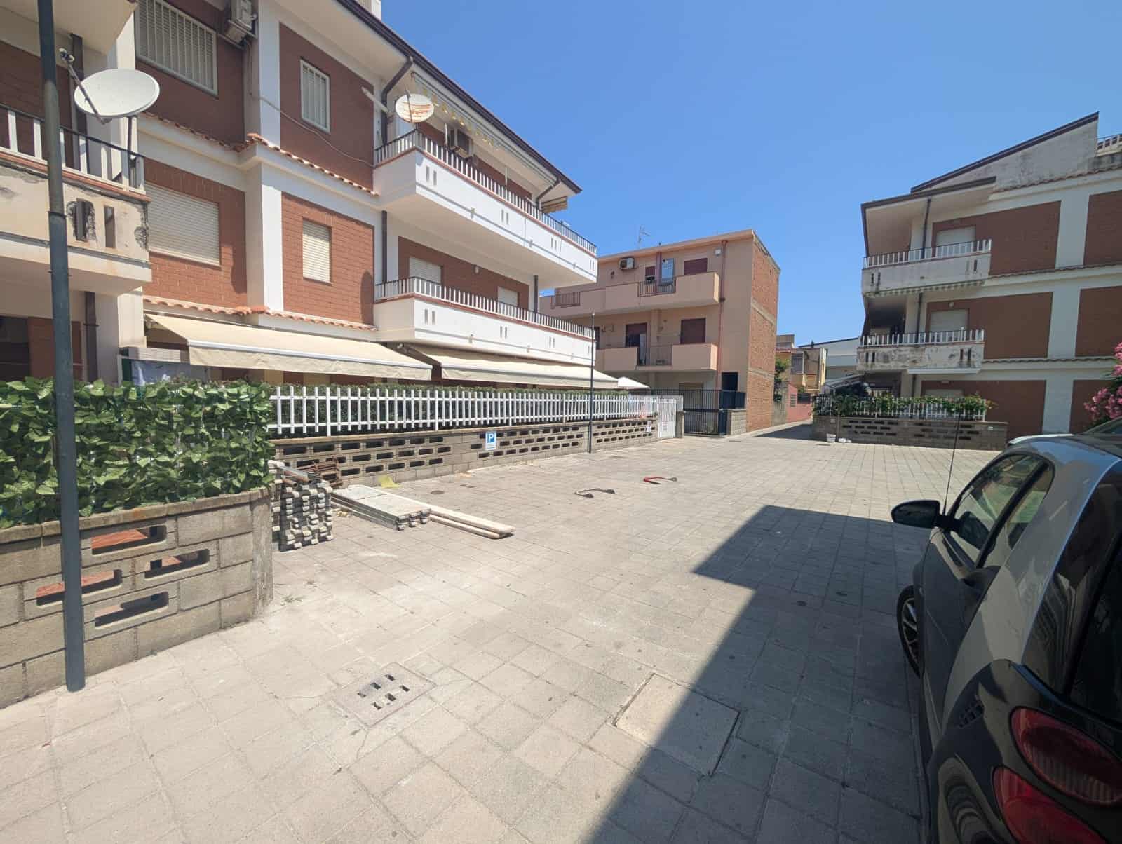 Vicolo condominiale con parcheggio e edifici residenziali, spazio esterno in zona urbana, parcheggio privato, appartamenti con balconi, ambiente tranquillo e ben curato.