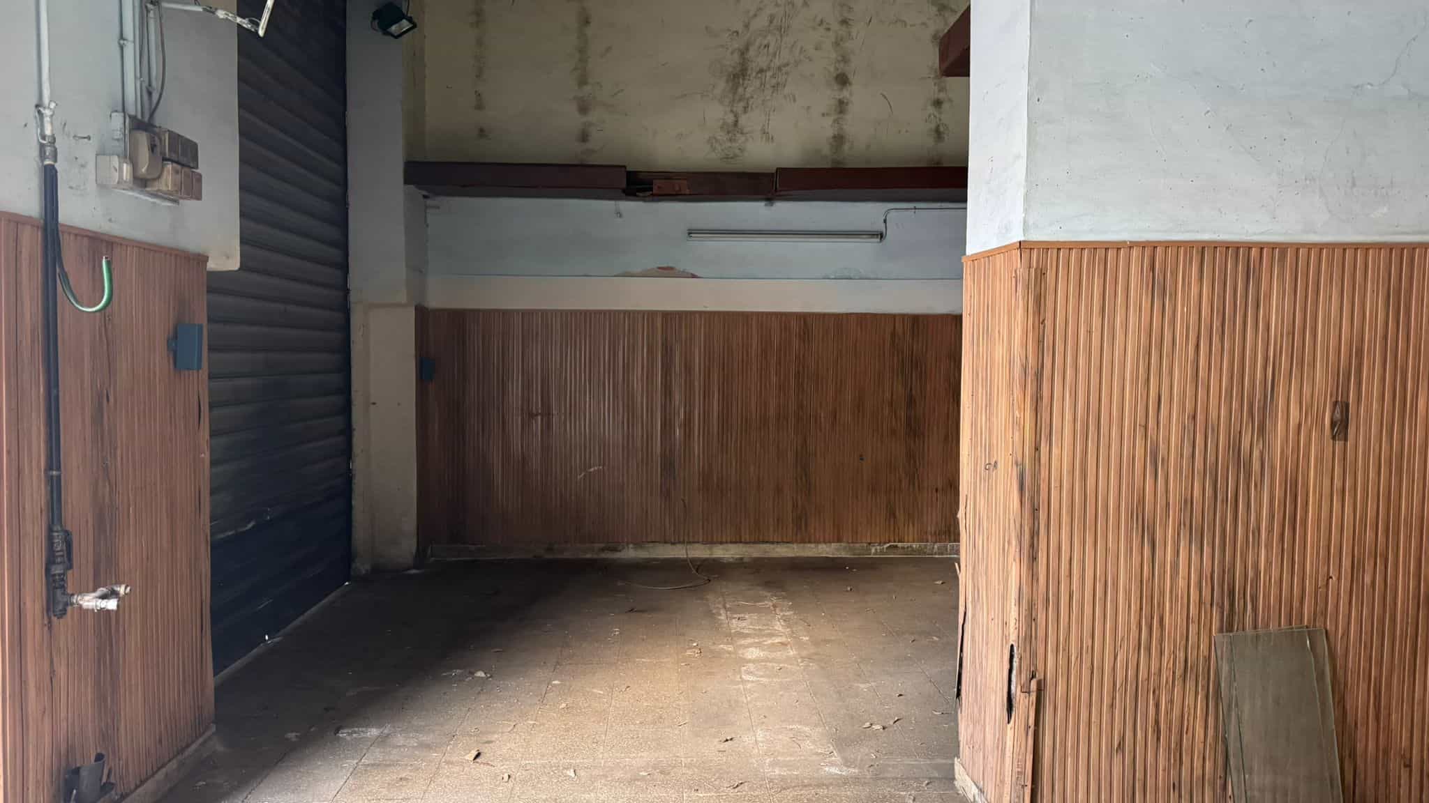 Spazio garage in un'area urbana, con pareti in legno e pavimento in cemento, ideale per parcheggio e deposito.
