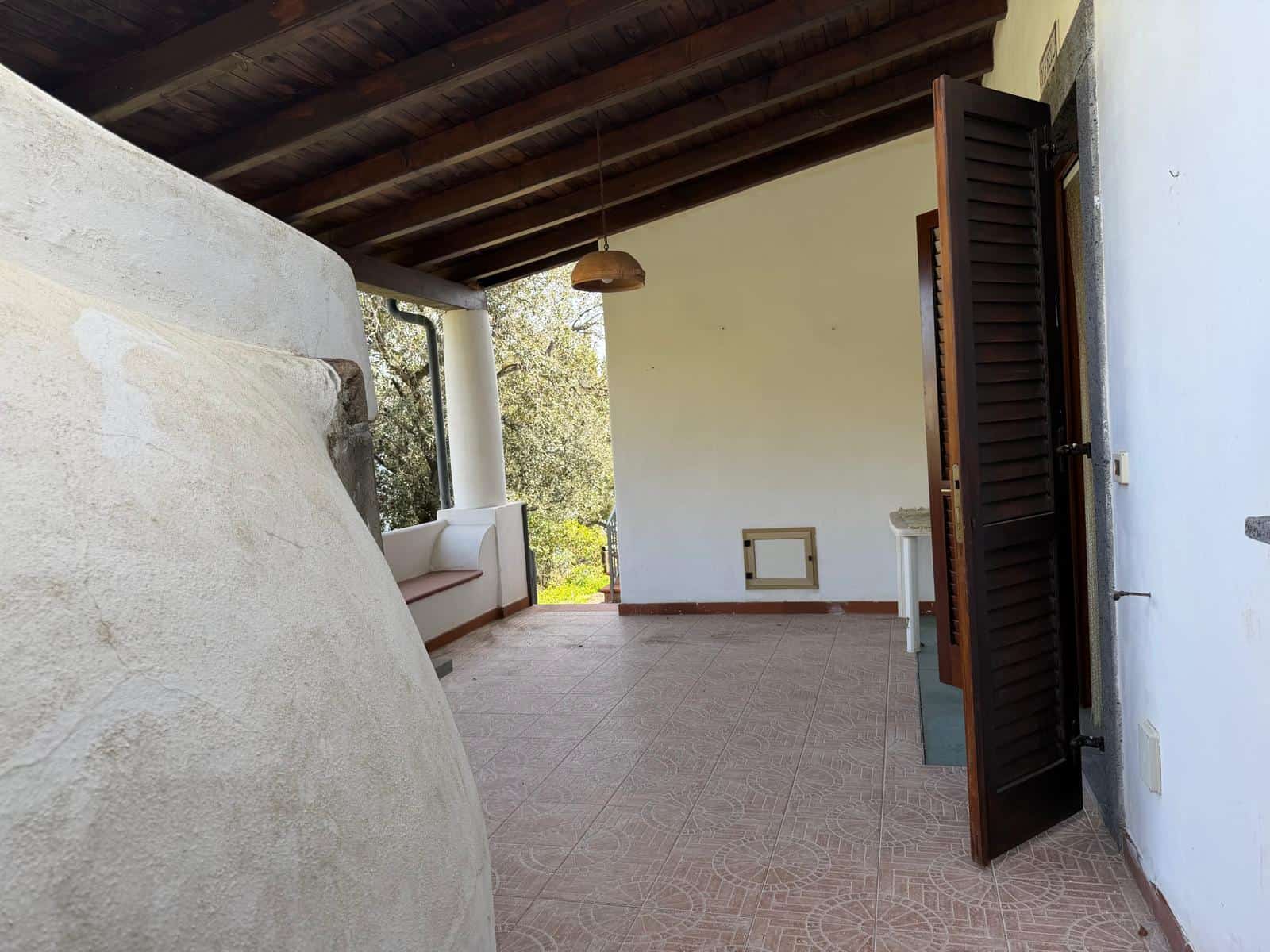 Aggiungi un'immagine di un'ampia terrazza o veranda con vista sulla natura, con pareti bianche, pavimento in piastrelle e un soffitto in legno, ideale per relax e convivialità all'aperto.