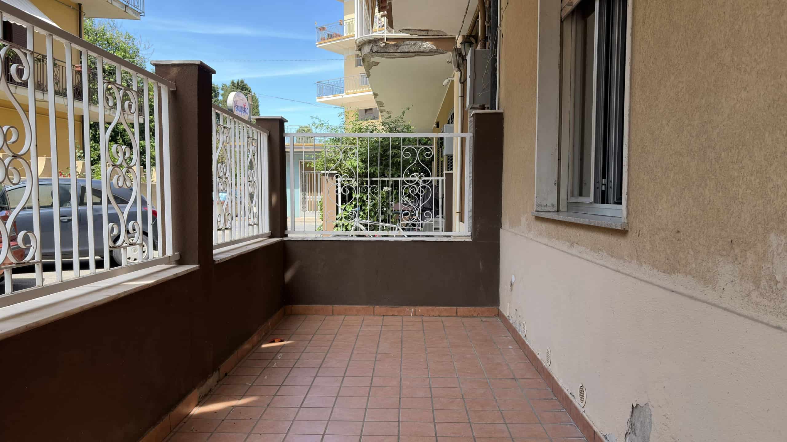 Balcone di un appartamento con pavimento in piastrelle e ringhiera in ferro battuto, vista su strada e edifici circostanti.