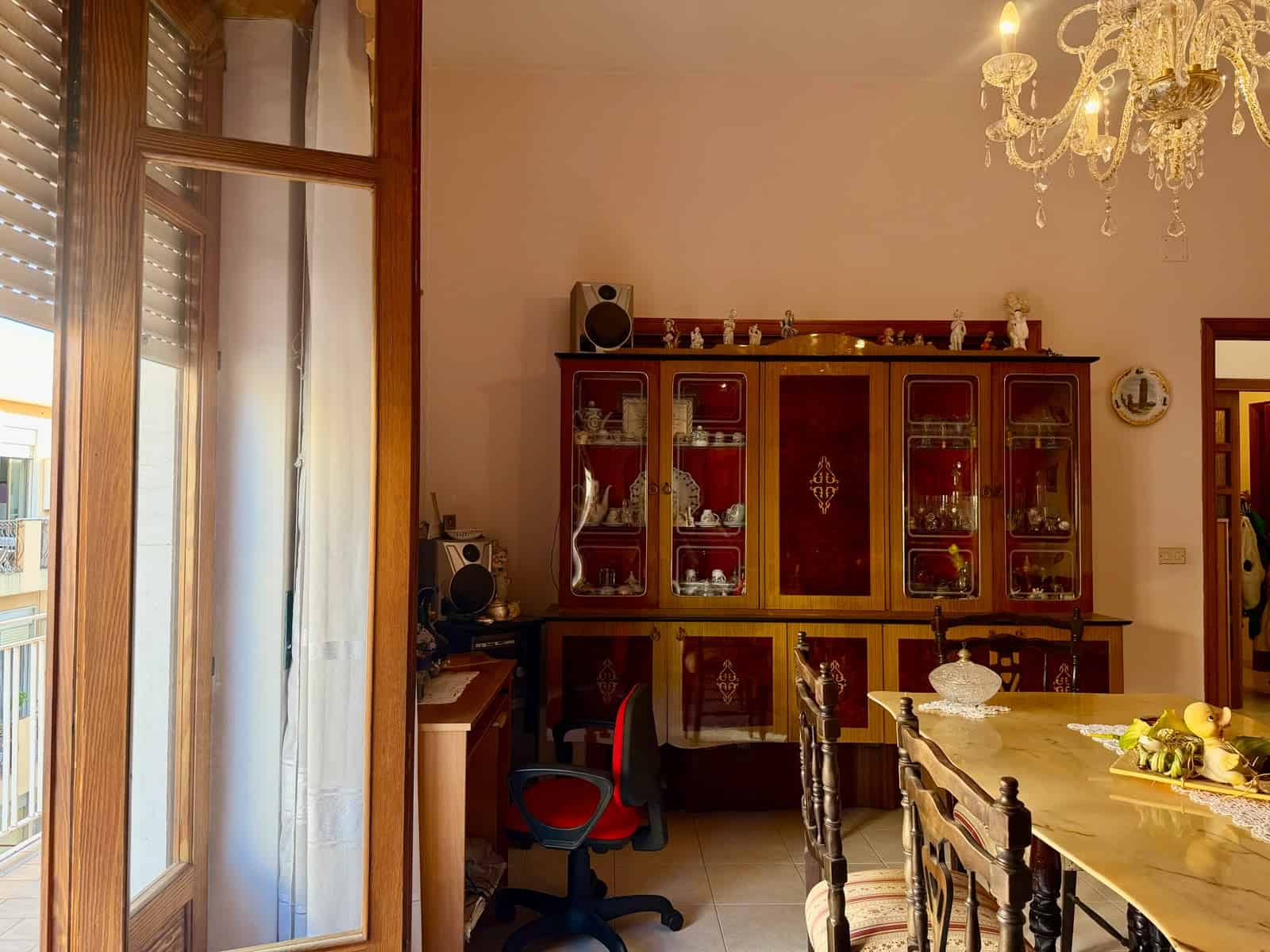Interno di un appartamento con mobili classici, grande vetrina e lampadario elegante.