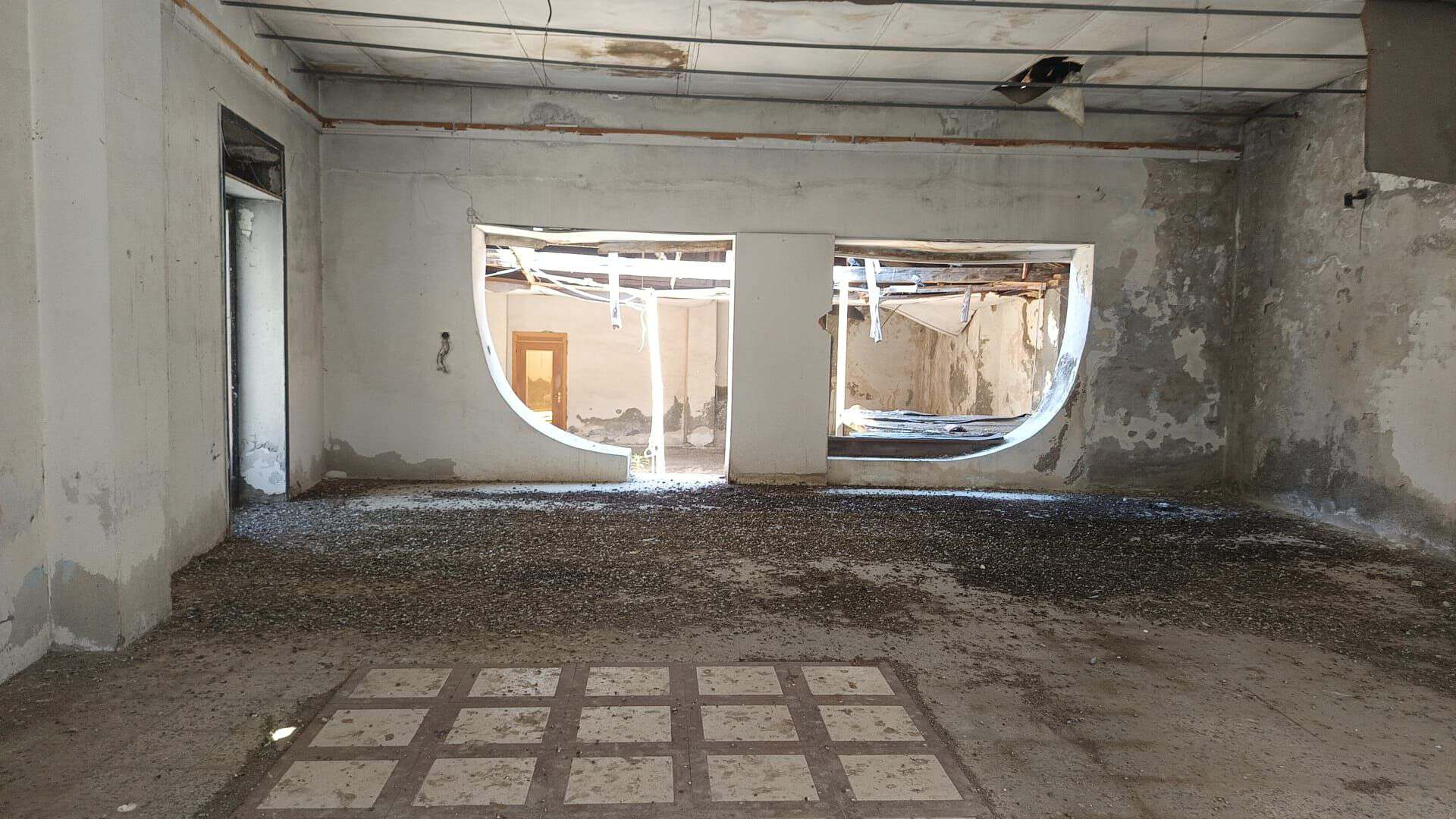 Interno di un locale commerciale in vendita con pareti in cemento e grandi finestre rotonde.