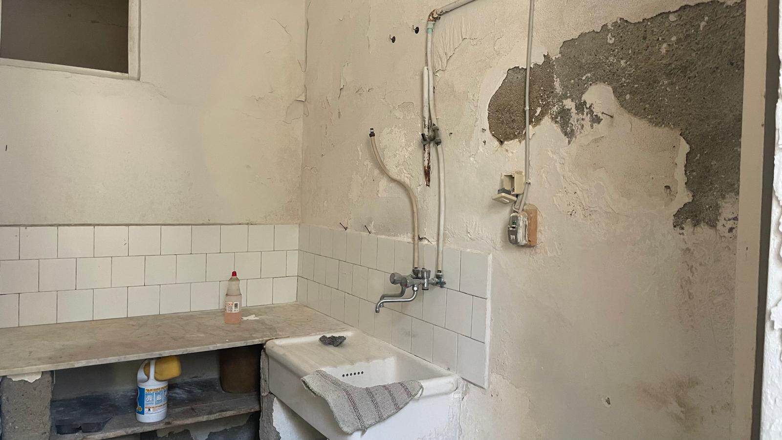 Immagine di una cucina in fase di ristrutturazione con pareti danneggiate e impianto idraulico visibile.