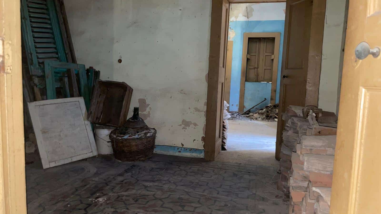 Interno di una casa in fase di ristrutturazione con pareti danneggiate e materiali da costruzione.
