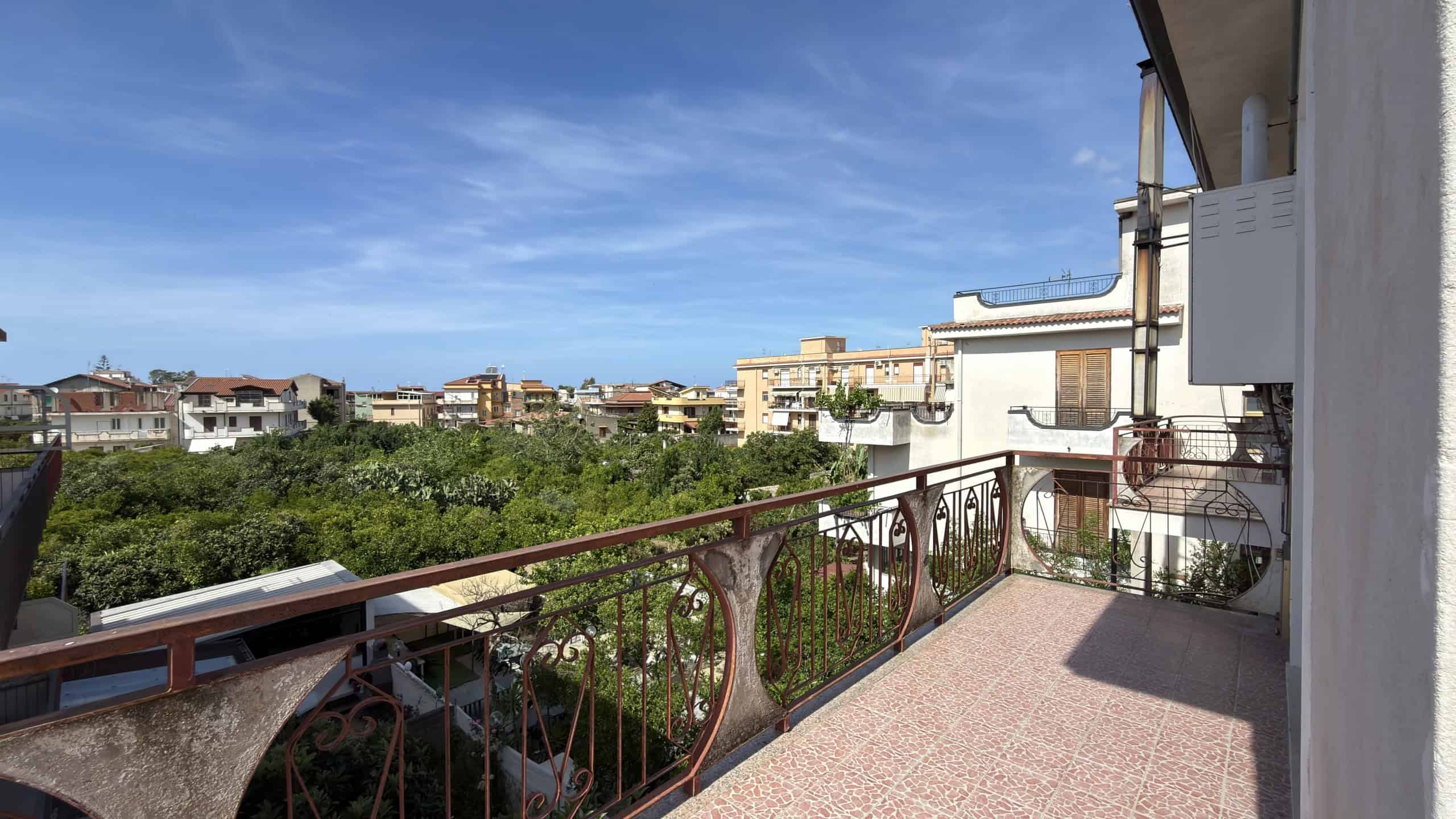 Balcone di un appartamento con vista sulla città e sul verde, con ringhiera in ferro battuto e pavimento in piastrelle.
