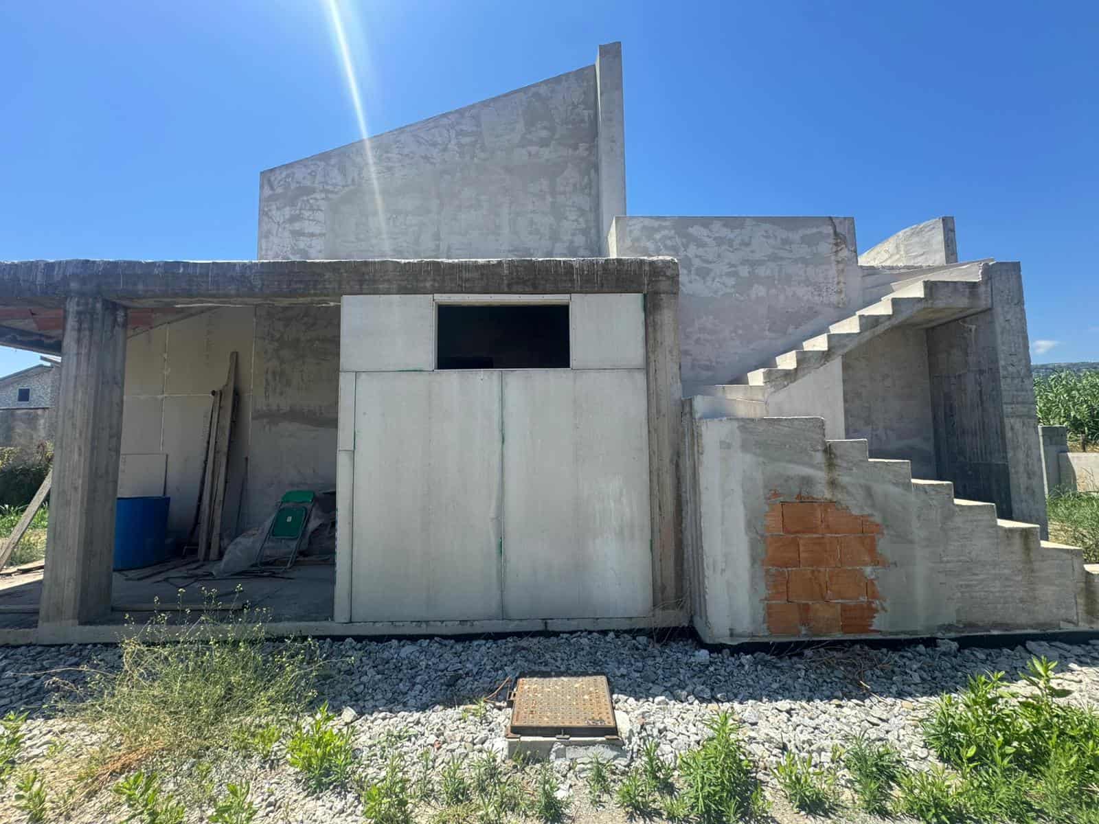 Edificio in costruzione con scale esterne e pareti in cemento sotto un cielo azzurro.