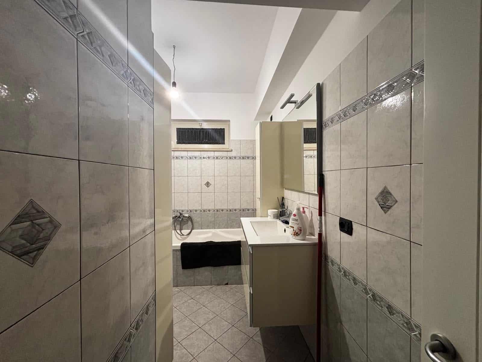 Bagno moderno con piastrelle chiare e dettagli decorativi, lavabo e specchio.