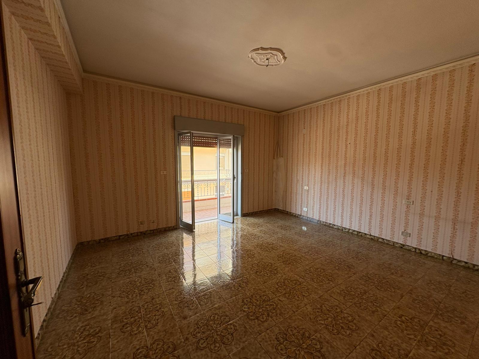 Ampio soggiorno vuoto con pareti a righe e balcone, ideale per appartamento in vendita a Merì.