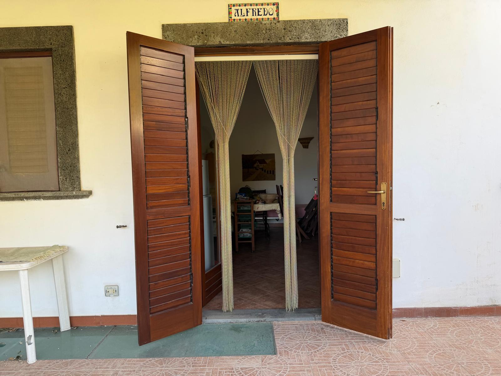ALETTA in legno aperta che conduce a un soggiorno con tende leggere e arredi visibili all'interno, in un ambiente domestico accogliente e luminoso.