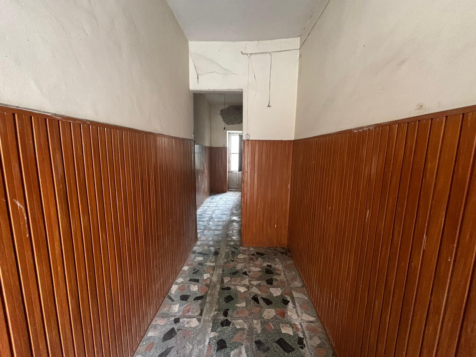 Passaggio stretto con pareti rivestite in legno e pavimento in piastrelle di marmo, in un edificio residenziale in fase di ristrutturazione.