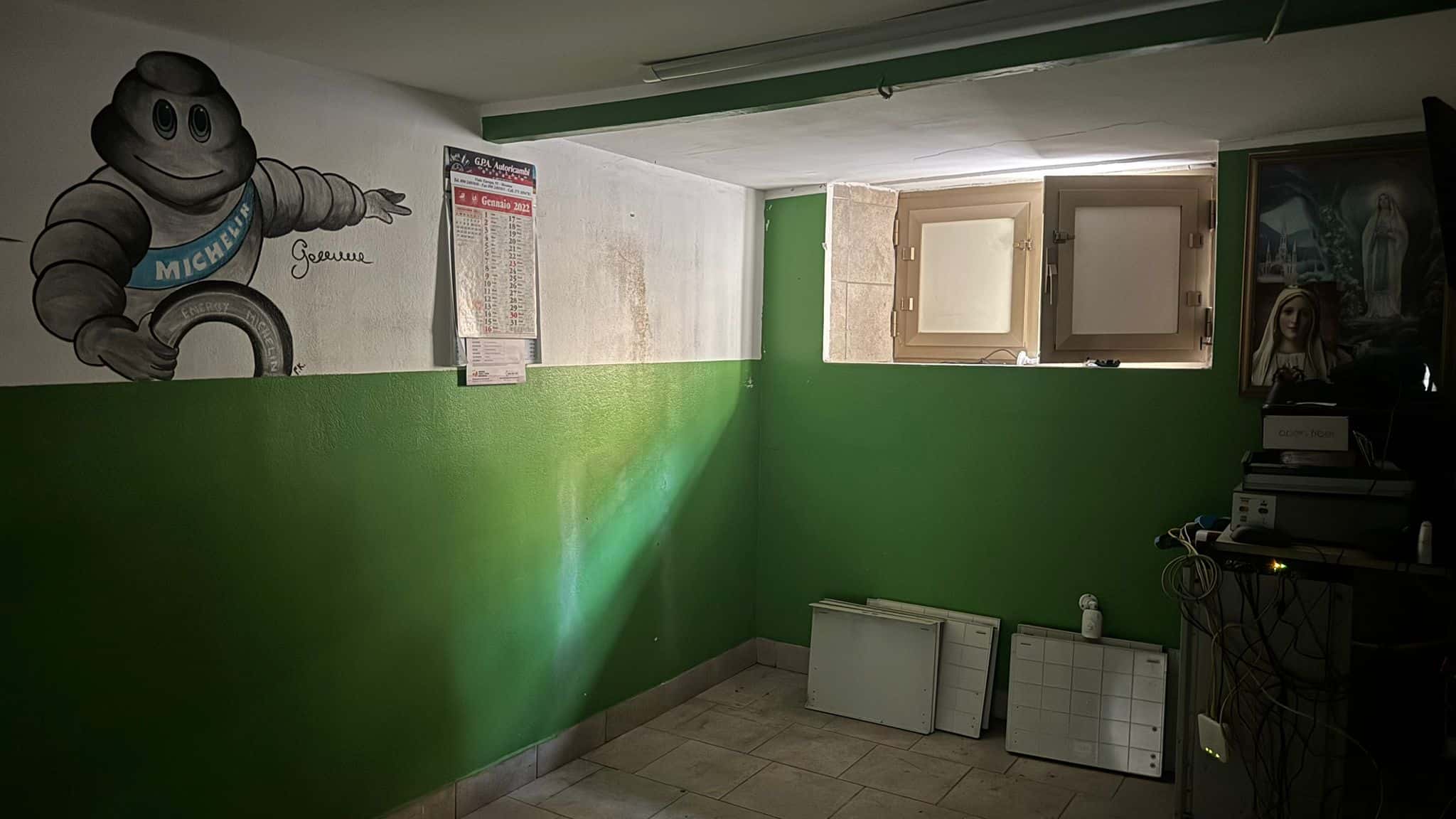 Interno di un appartamento con pareti verdi, finestra e arredamento semplice, pronto per essere ristrutturato o abitato.