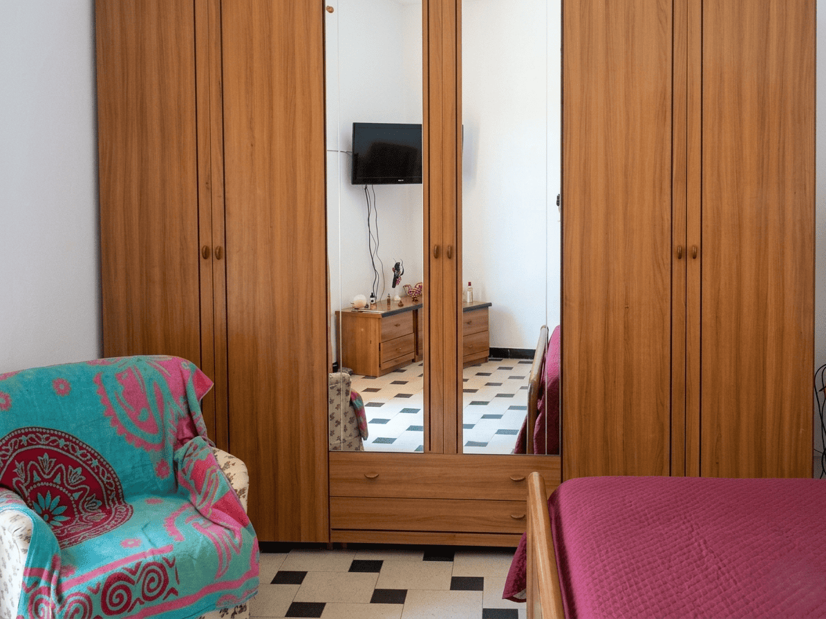 L'armadio a muro con ante in legno e specchio, in una camera da letto moderna, con un divano colorato e un televisore a parete.