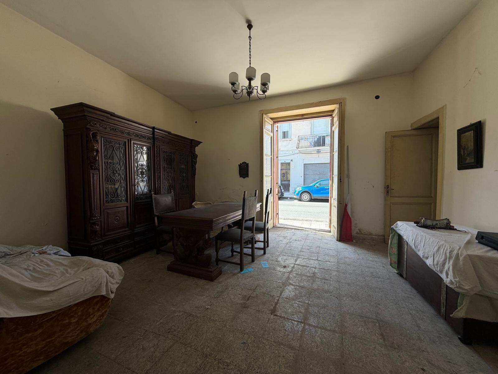 Interno di una casa indipendente in vendita a Barcellona P.G., soggiorno con arredi d'epoca e porta finestra che dà sulla strada.