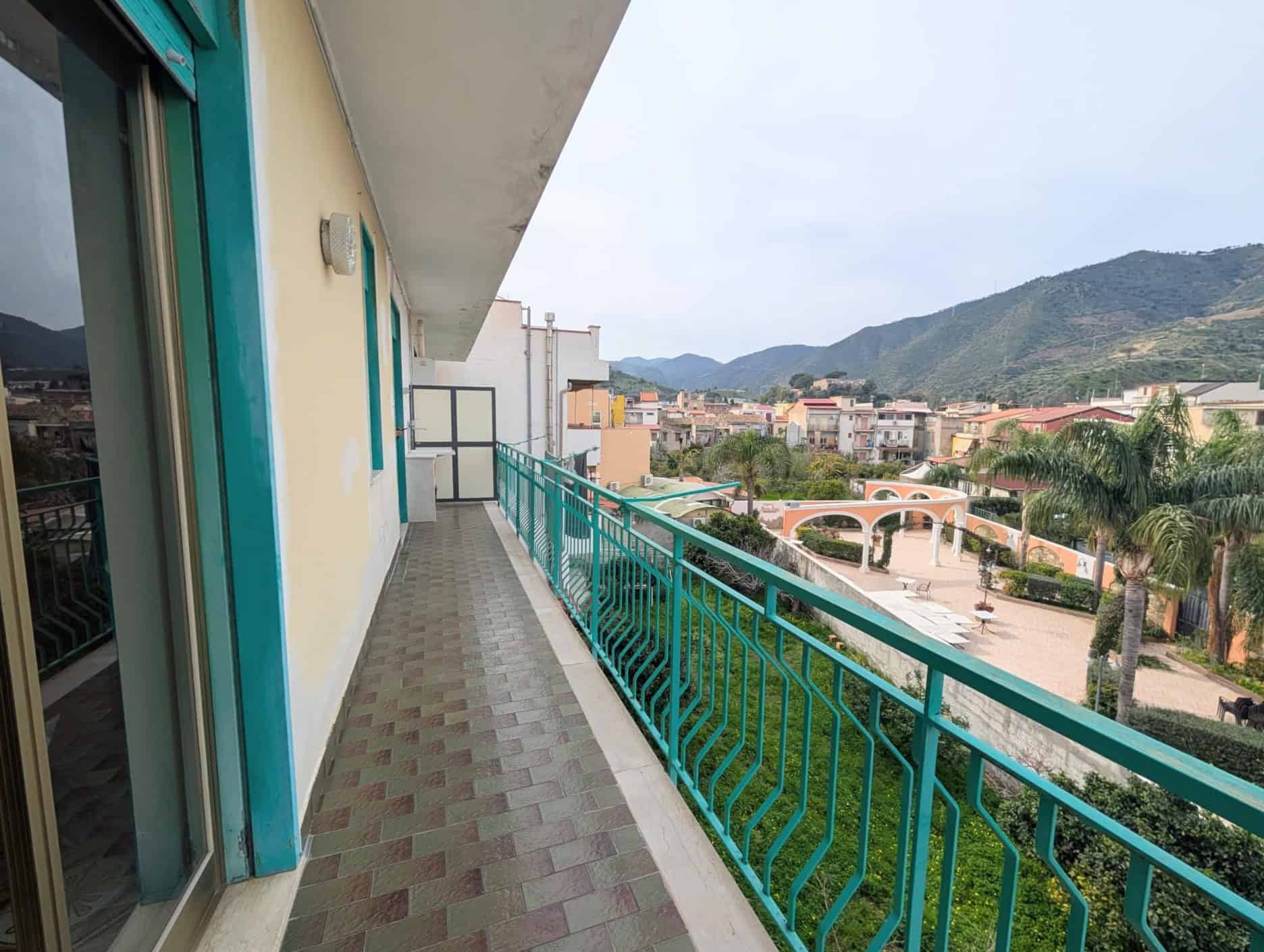 Balcone di un appartamento con vista panoramica sulle montagne e sulla città, con ringhiera verde e pavimentazione in piastrelle.