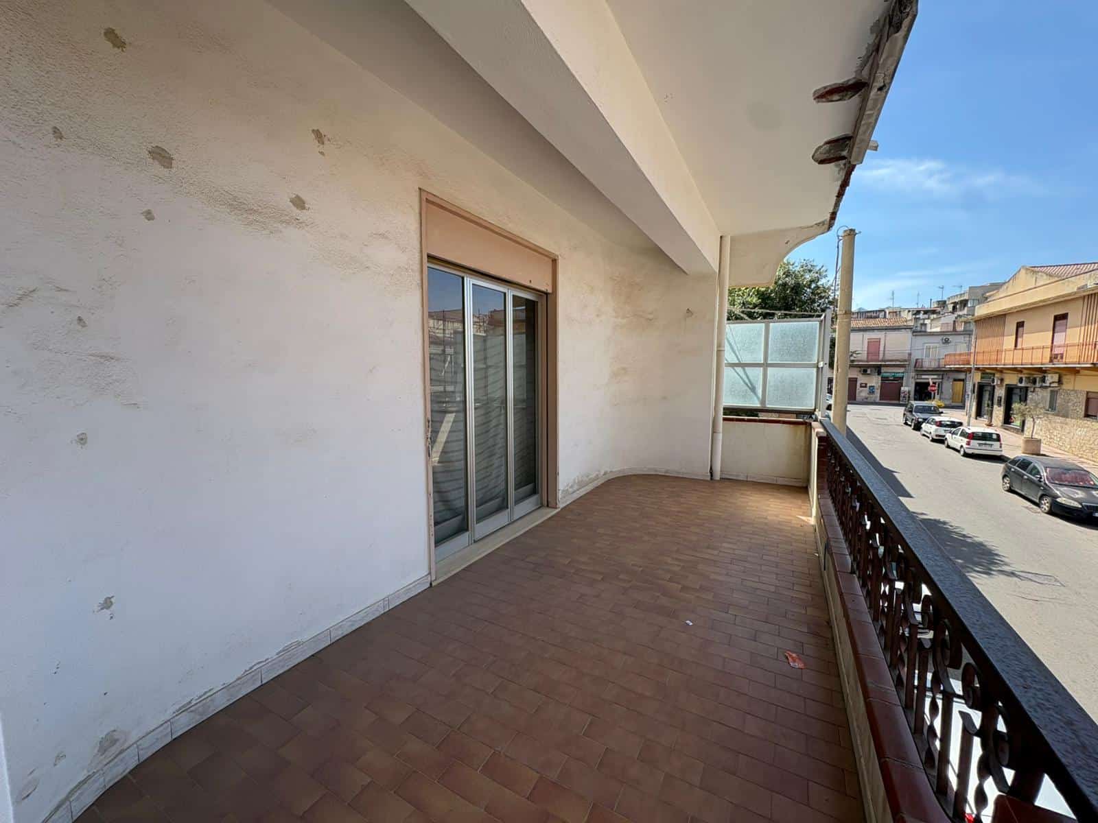 Balcone di un appartamento in vendita a Merì con vista sulla strada e edifici circostanti.