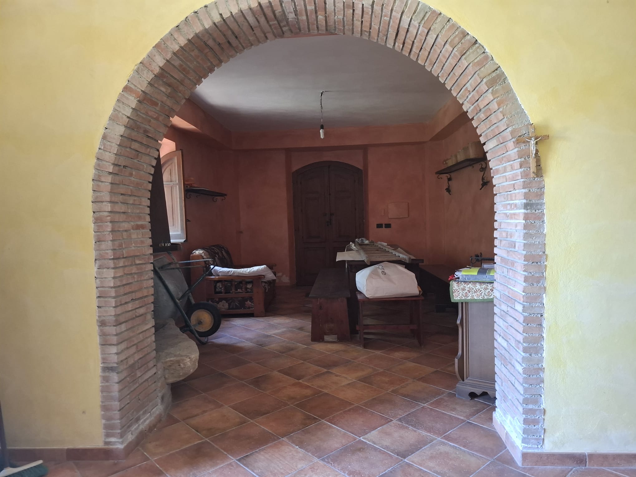 Interno di una casa rustica con pareti color pesca, archi in mattoni e mobili in legno, ambiente accogliente e tradizionale.