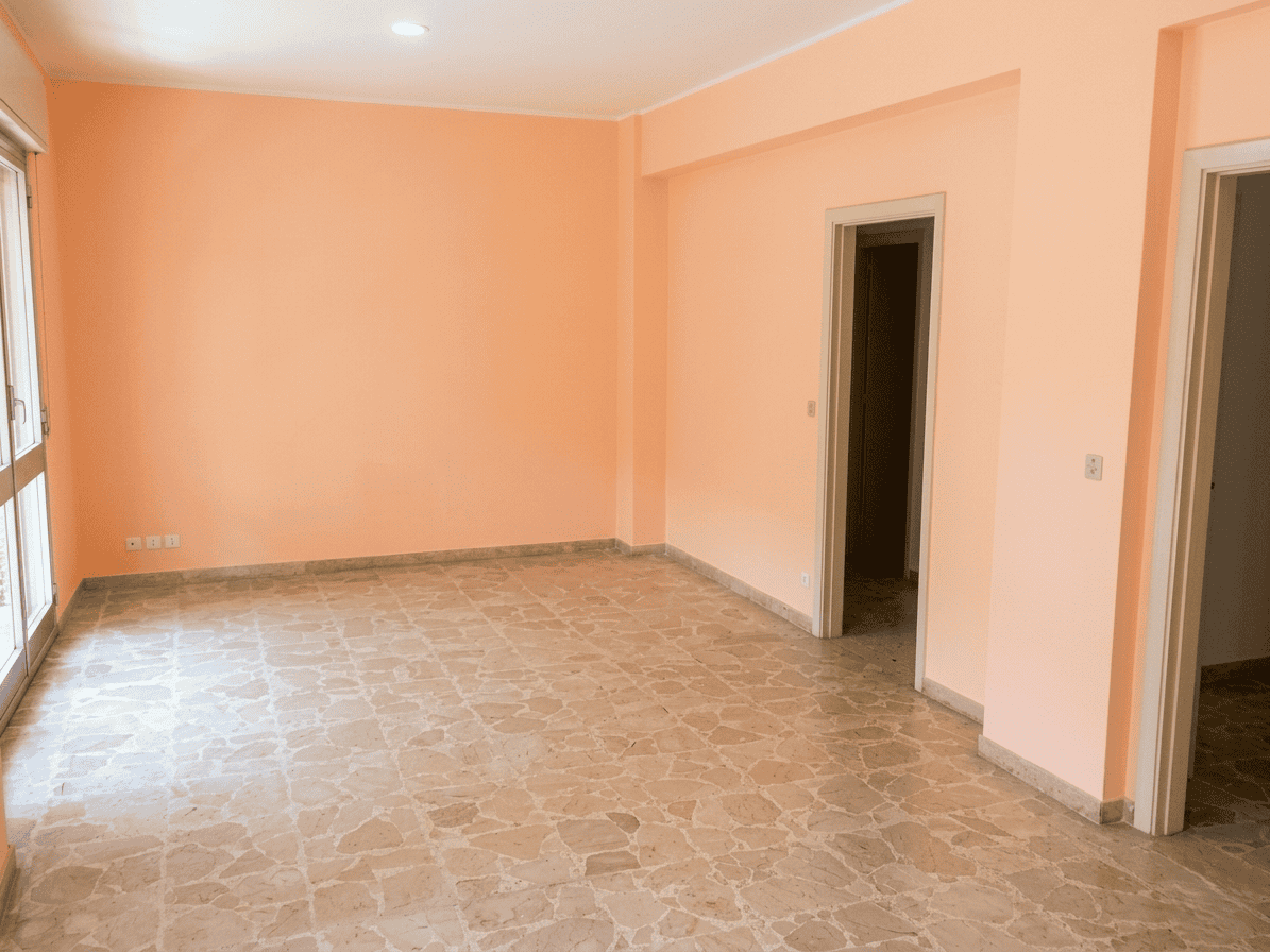 Vano soggiorno luminoso e spazioso con pareti color pesca e pavimento in piastrelle beige, ideale per arredare con mobili moderni e creare un ambiente accogliente.