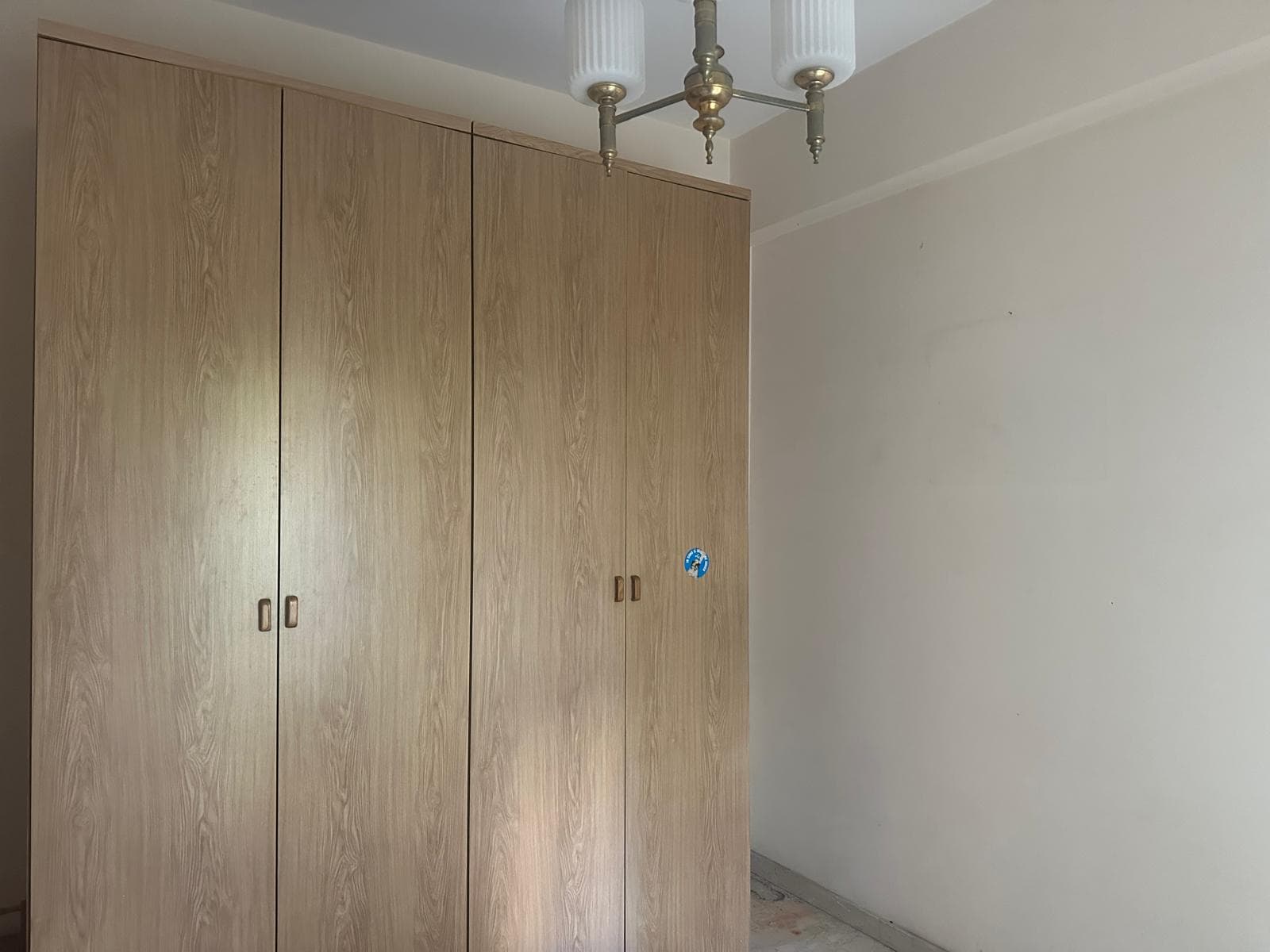 Armadio a muro in legno chiaro in una stanza luminosa con pareti bianche e soffitto decorato, illuminata da lampadario classico. Ideale per arredamento funzionale e moderno.