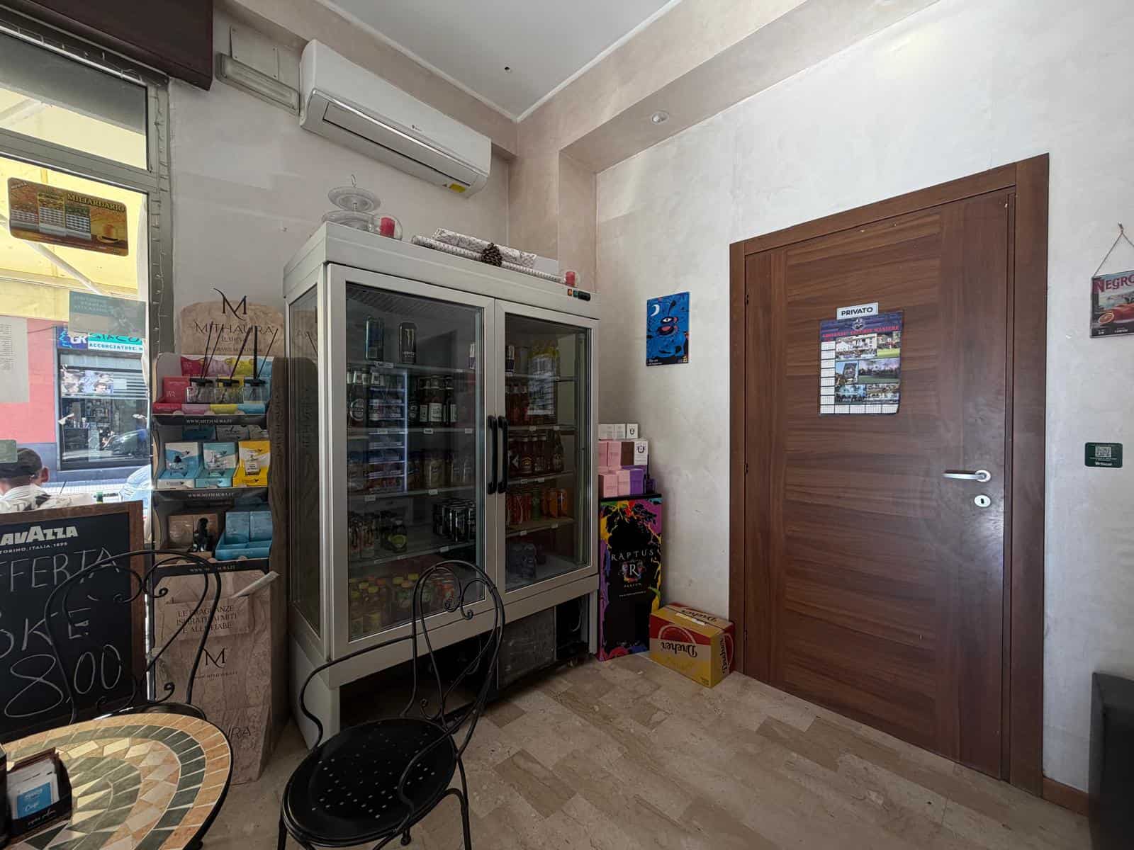Interno di un negozio con frigorifero e scaffali pieni di prodotti, porta in legno e decorazioni colorate.