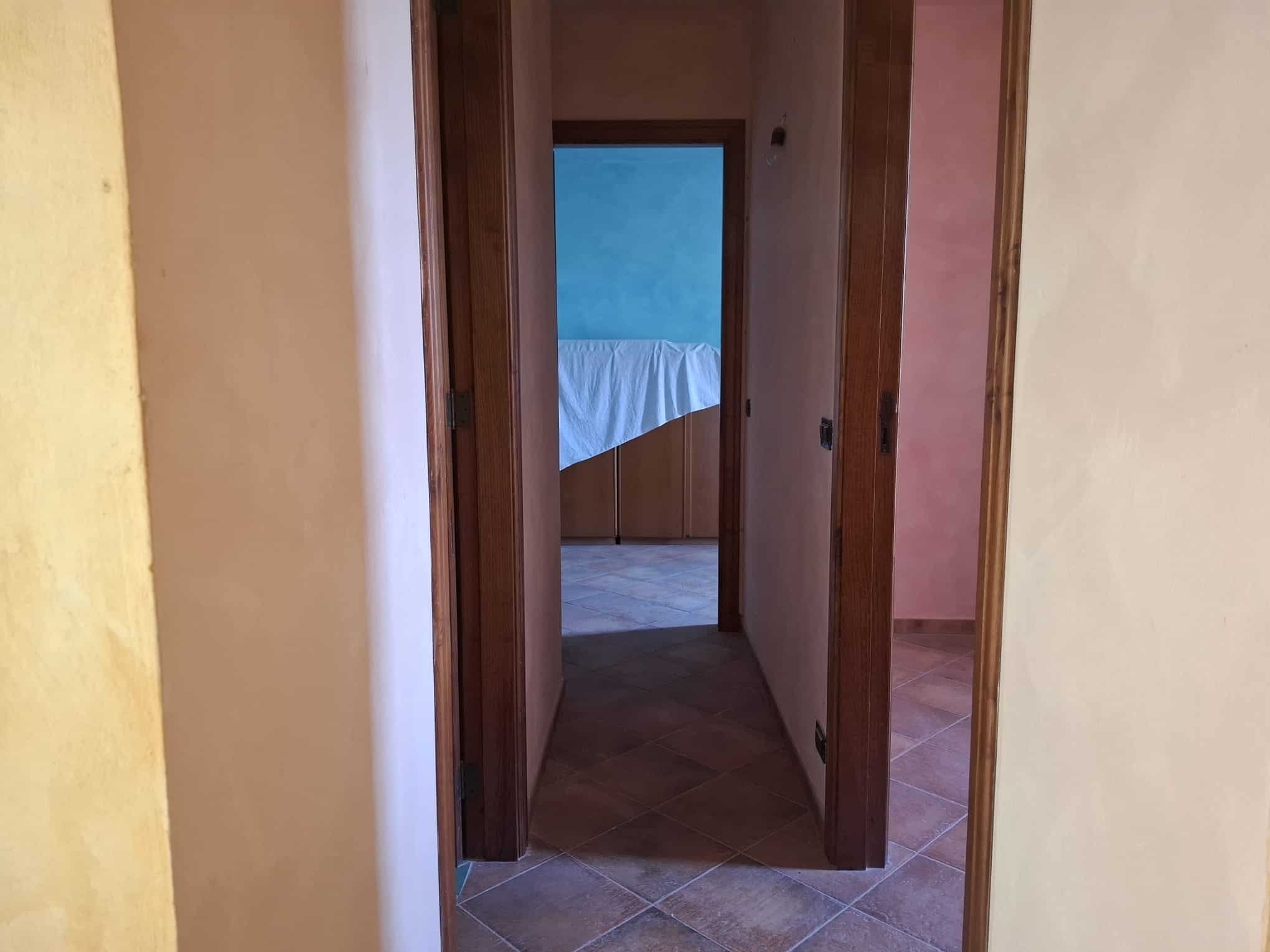 Corridoio interno di una casa con pareti colorate e pavimento in piastrelle, vista verso una stanza con pareti azzurre e letto.